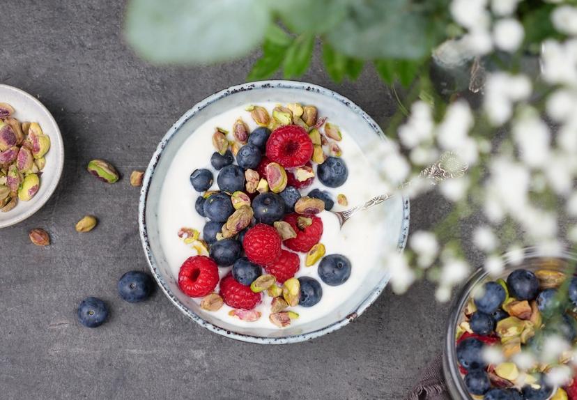 Dame og jente som sitter ved siden av hverandre i en sofa og smiler og spiser yoghurt.