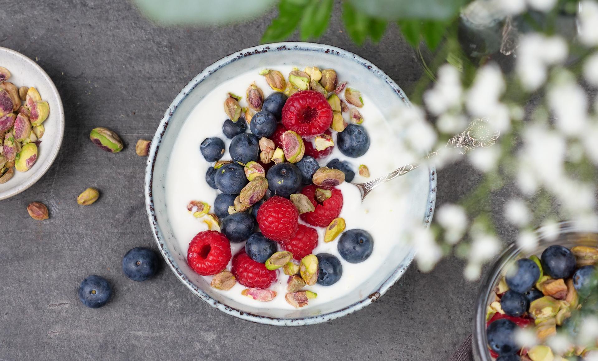 Skål med yoghurt, toppet med bringebær, blåbær og pistasjenøtter