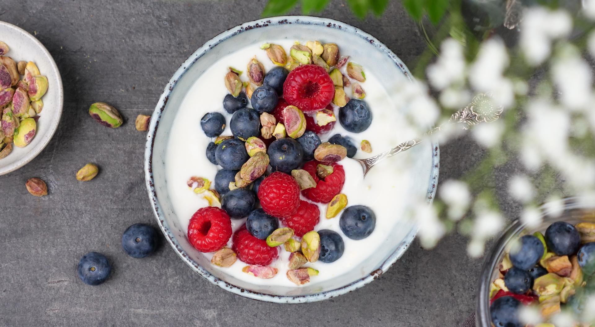 Skål med yoghurt, toppet med bringebær, blåbær og pistasjenøtter