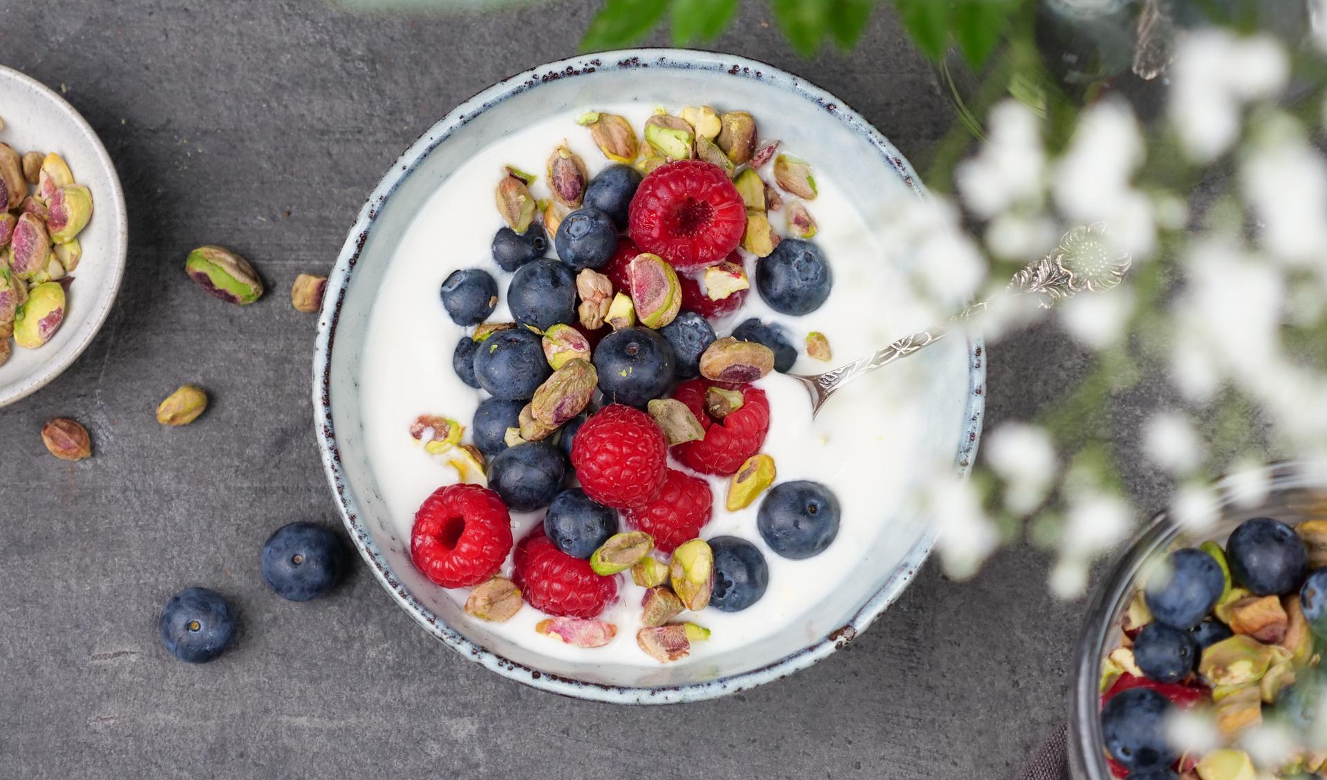 Skål med yoghurt, toppet med bringebær, blåbær og pistasjenøtter