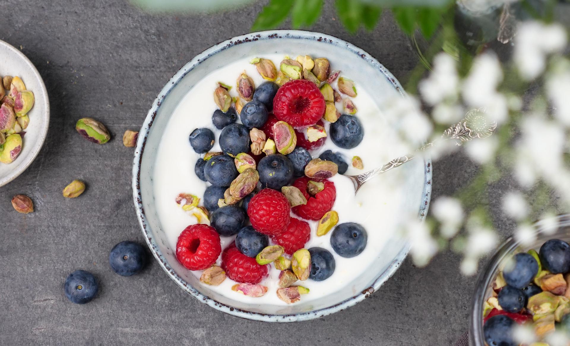 Skål med yoghurt, toppet med bringebær, blåbær og pistasjenøtter