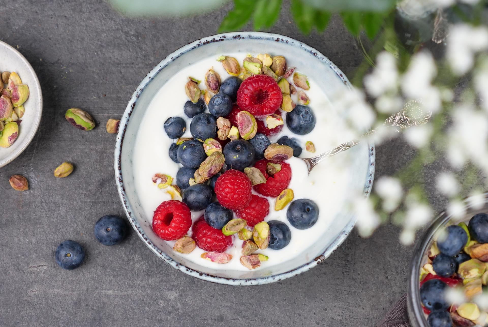 Skål med yoghurt, toppet med bringebær, blåbær og pistasjenøtter
