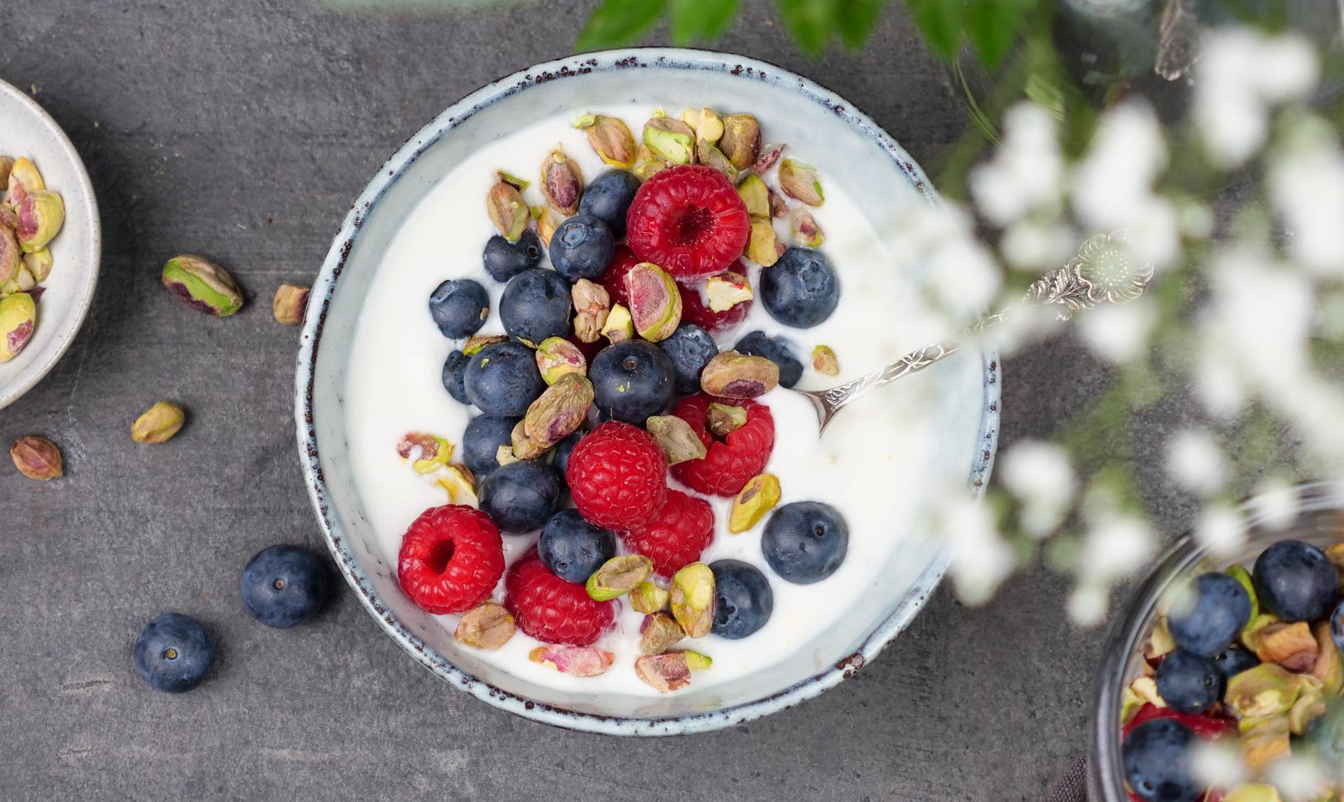 Skål med yoghurt, toppet med bringebær, blåbær og pistasjenøtter
