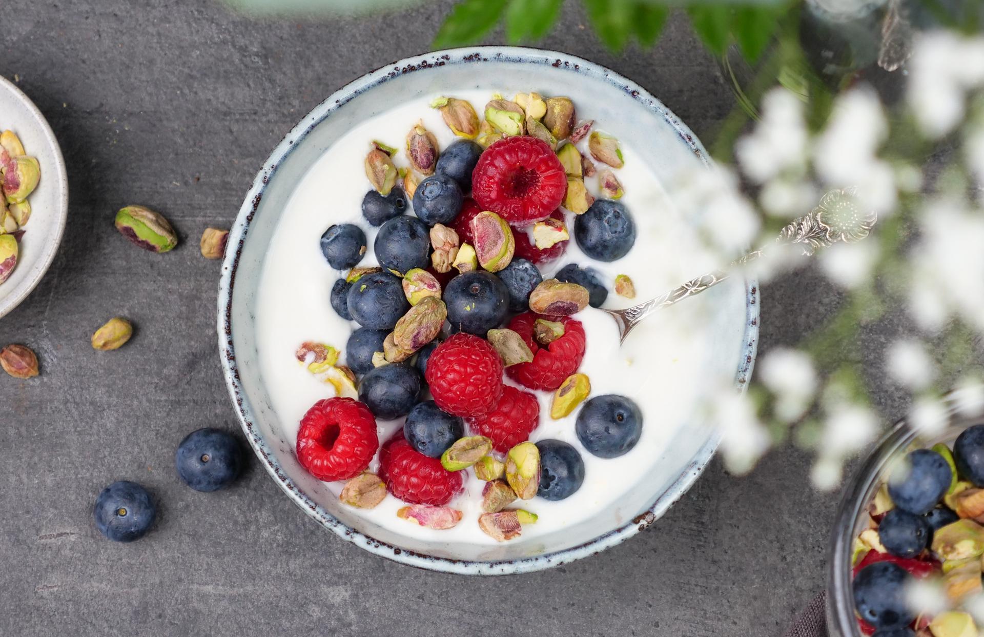 Skål med yoghurt, toppet med bringebær, blåbær og pistasjenøtter