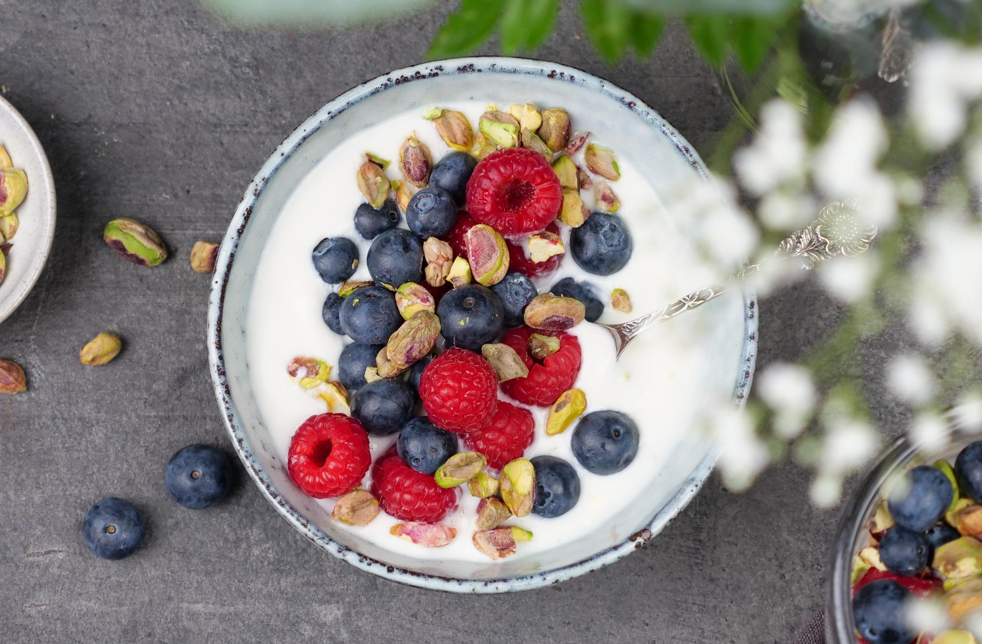 Skål med yoghurt, toppet med bringebær, blåbær og pistasjenøtter