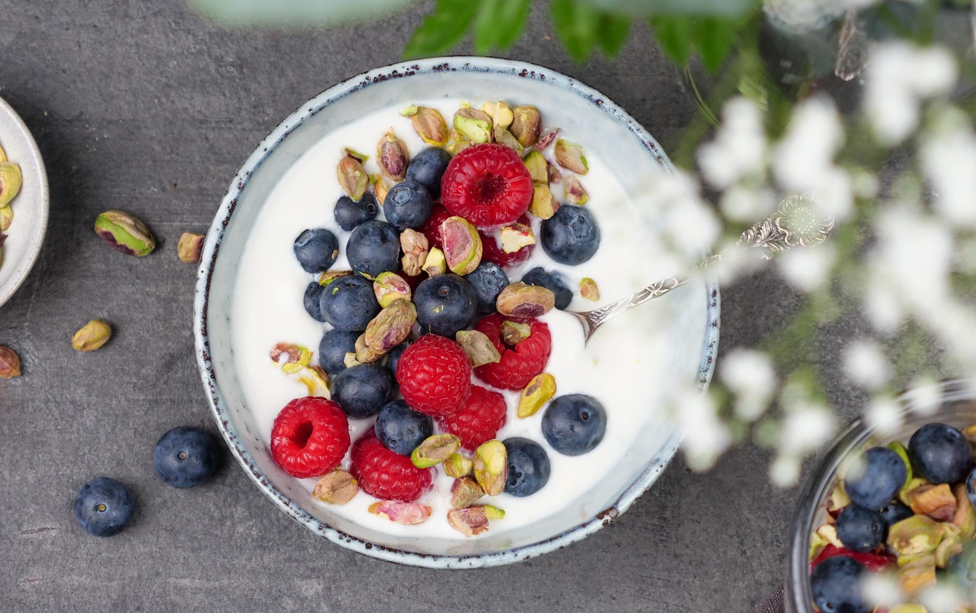 Skål med yoghurt, toppet med bringebær, blåbær og pistasjenøtter