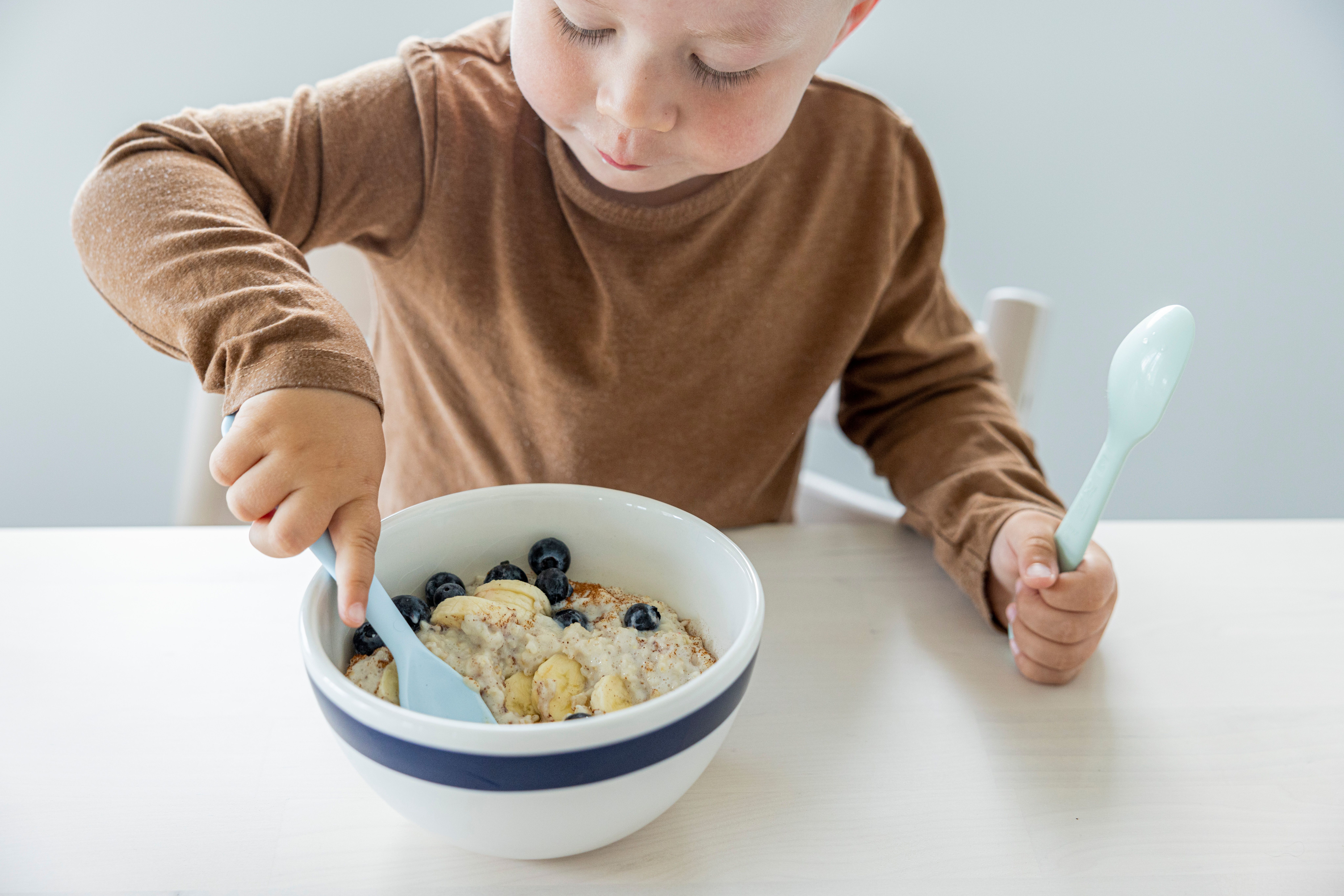 Liten gutt som spiser grøt med bær fra en skål. 