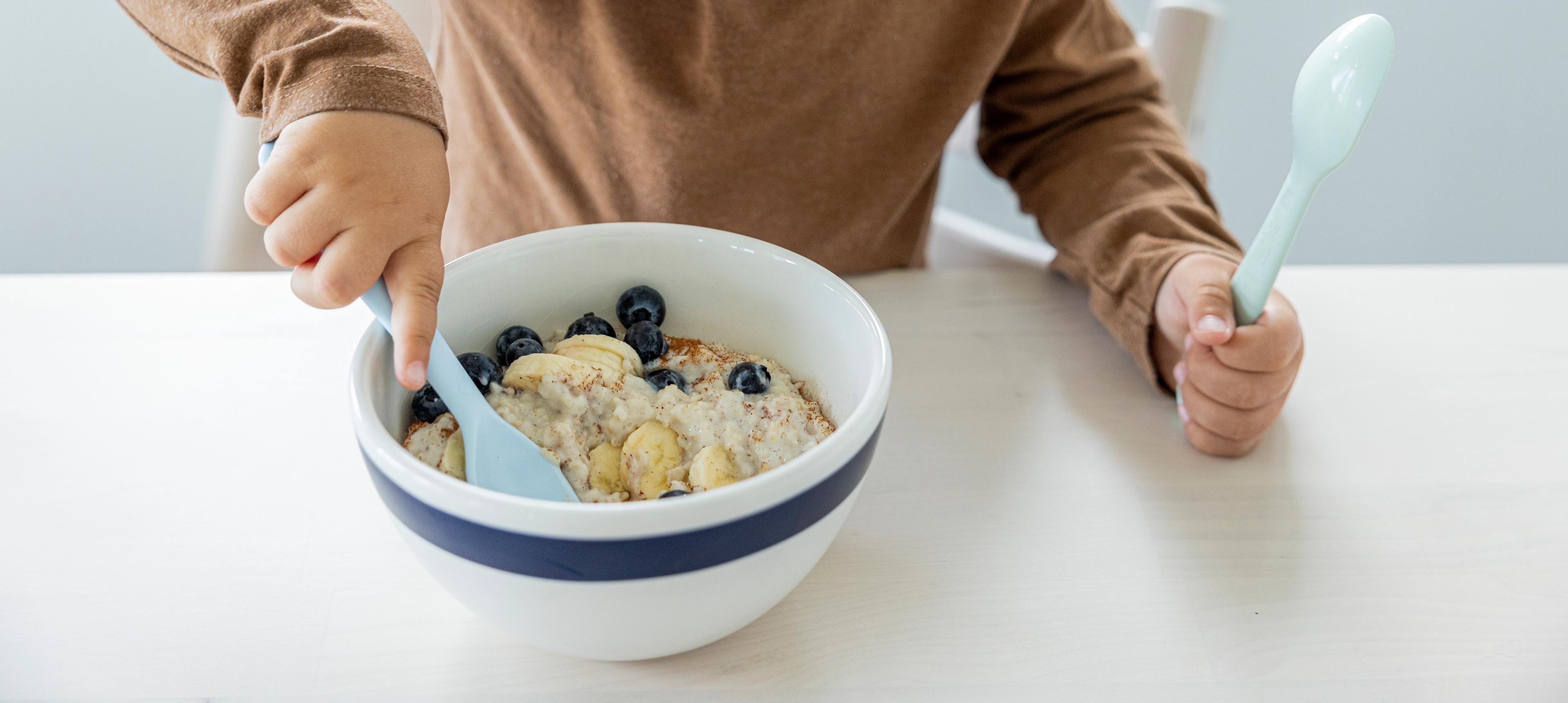 Liten gutt som spiser grøt med bær fra en skål.