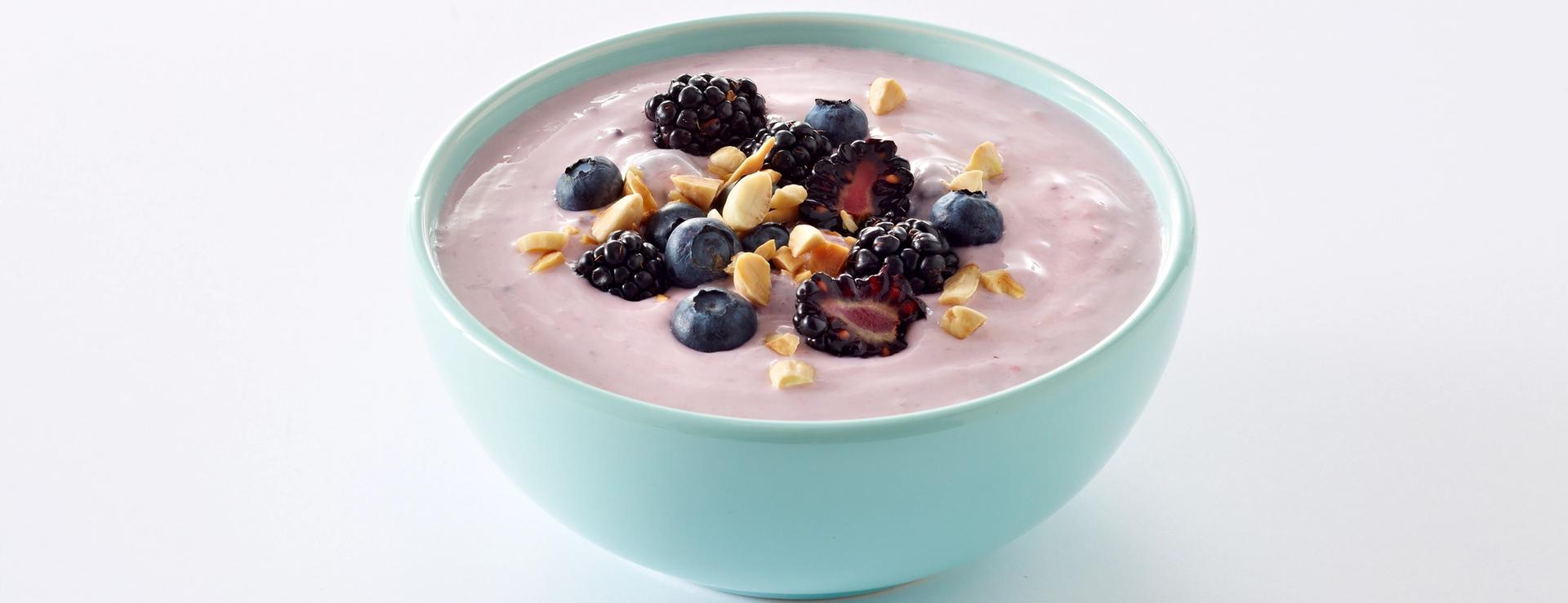 En turkis skål med yoghurt med bær og nøtter.