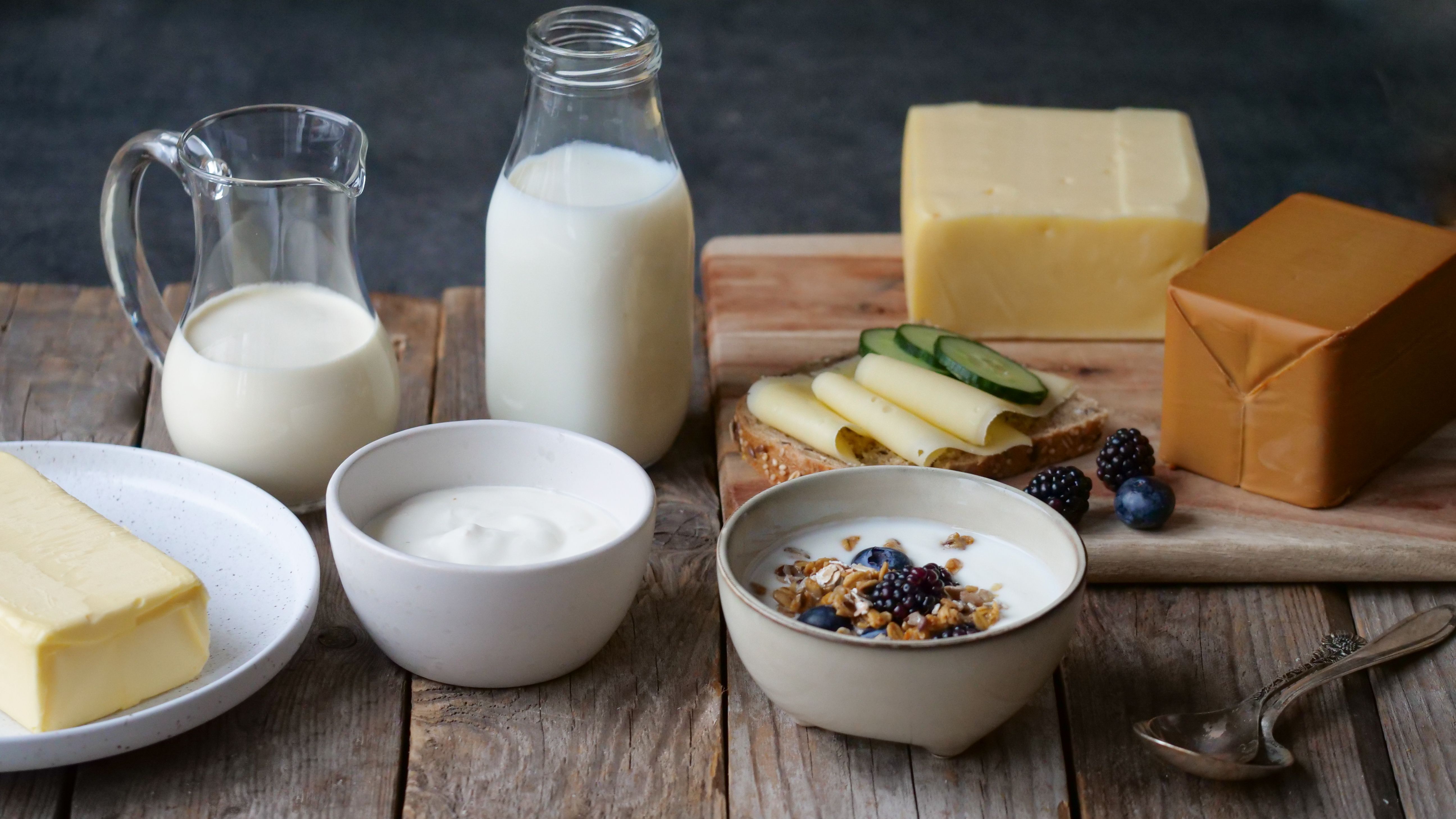 En rustikk fremstilling av melk, smør, gulost, brunost, yoghurt, frokostblanding med melk og fløte i en glasskanne. 