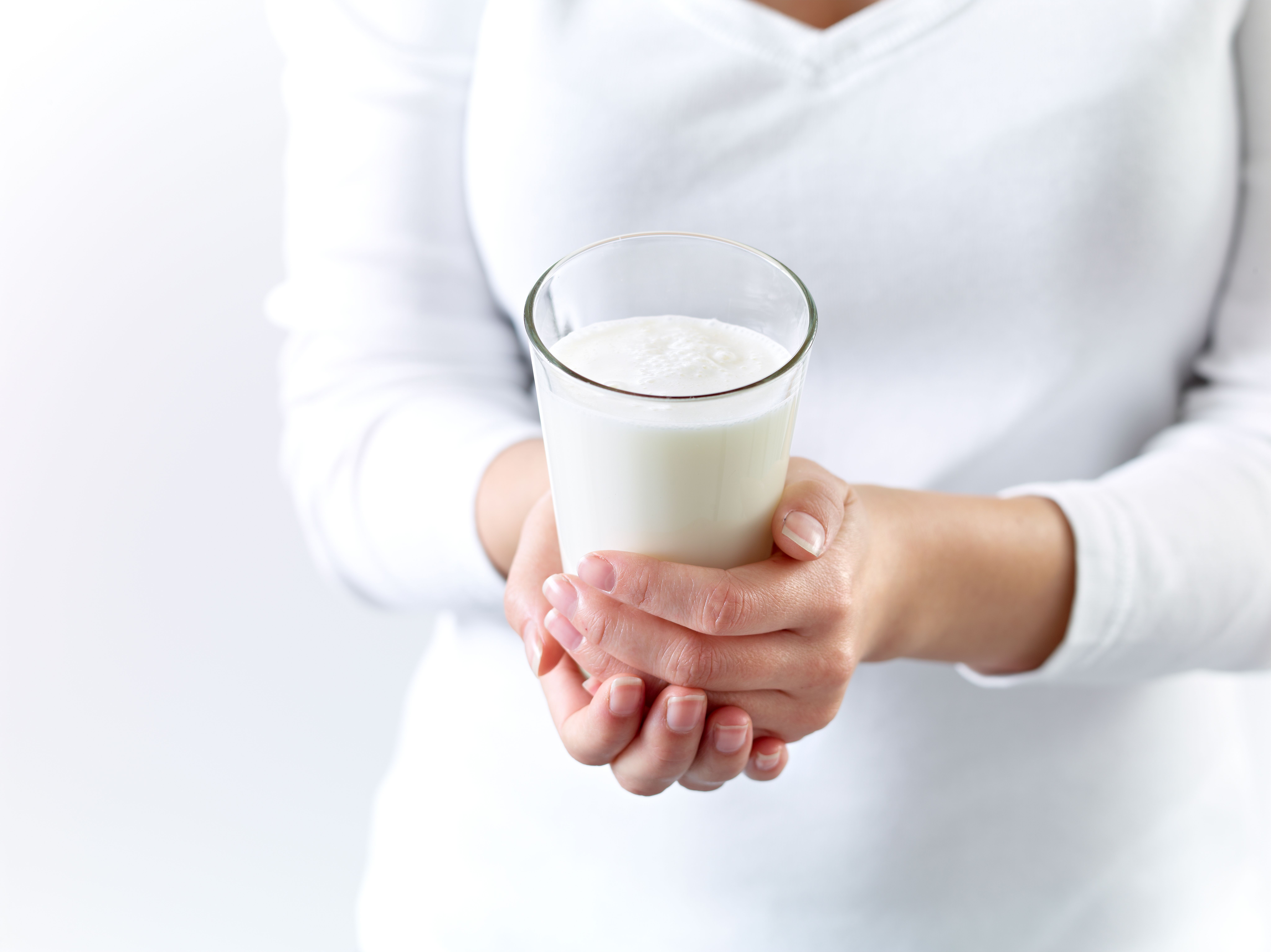 En dame i hvit genser som holder et glass melk.