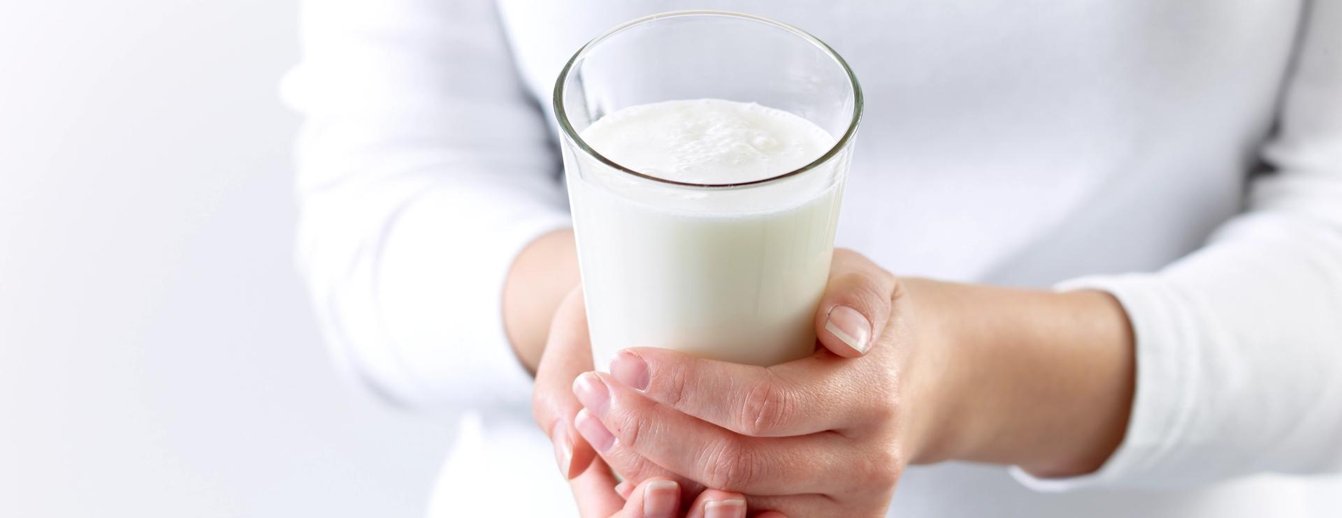 En dame i hvit genser som holder et glass melk.
