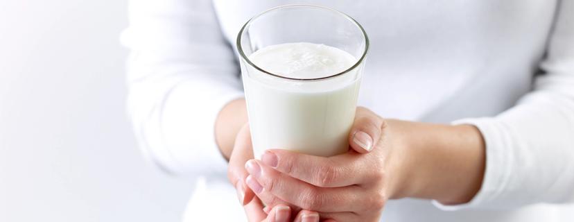 En dame i hvit genser som holder et glass melk.