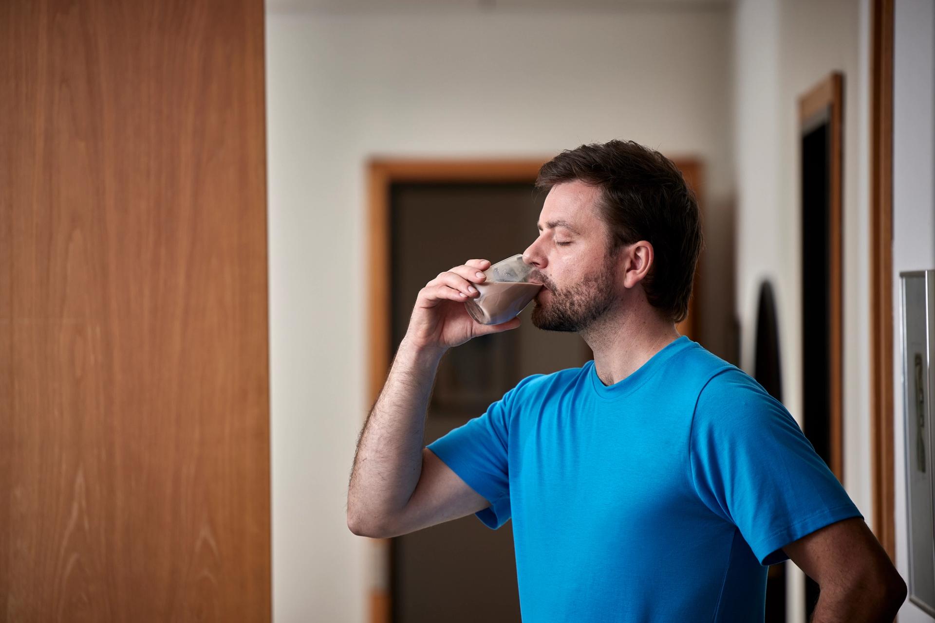 a man in a blue shirt is drinking a glass of milkshake .