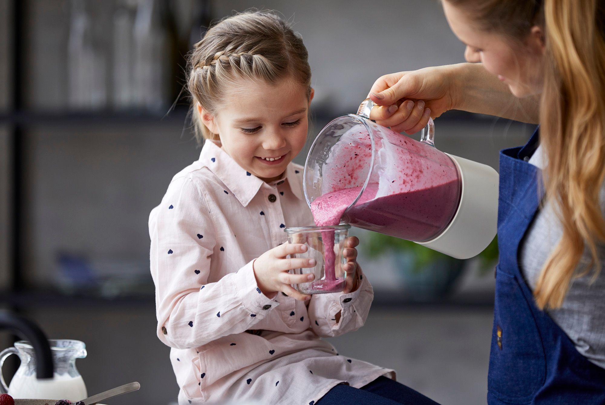 Jente som smiler mens en dame heller rosa smoothie i glasset hennes