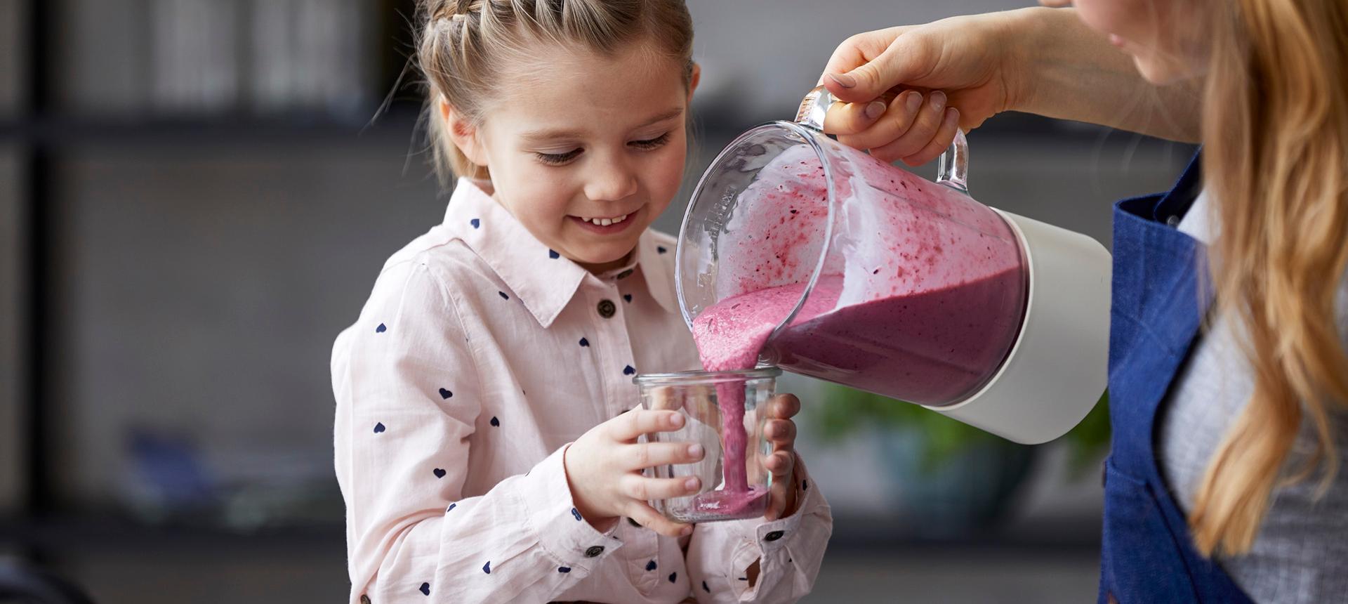 Jente som smiler mens en dame heller rosa smoothie i glasset hennes