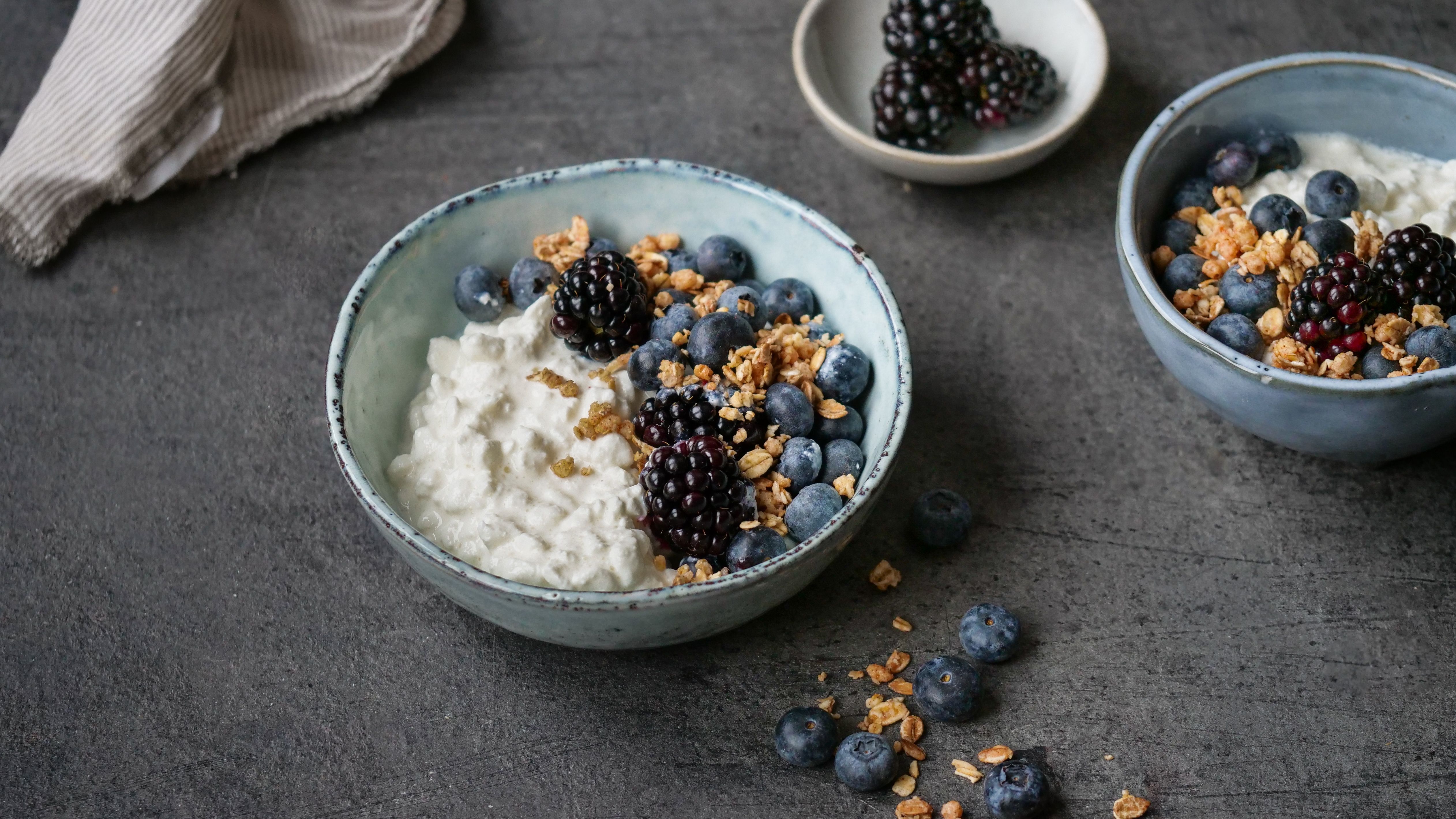 a bowl of yogurt with blueberries , blackberries and granola on a table .
