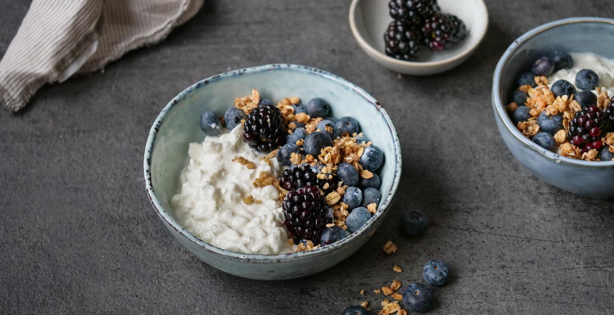 a bowl of yogurt with blueberries , blackberries and granola on a table .