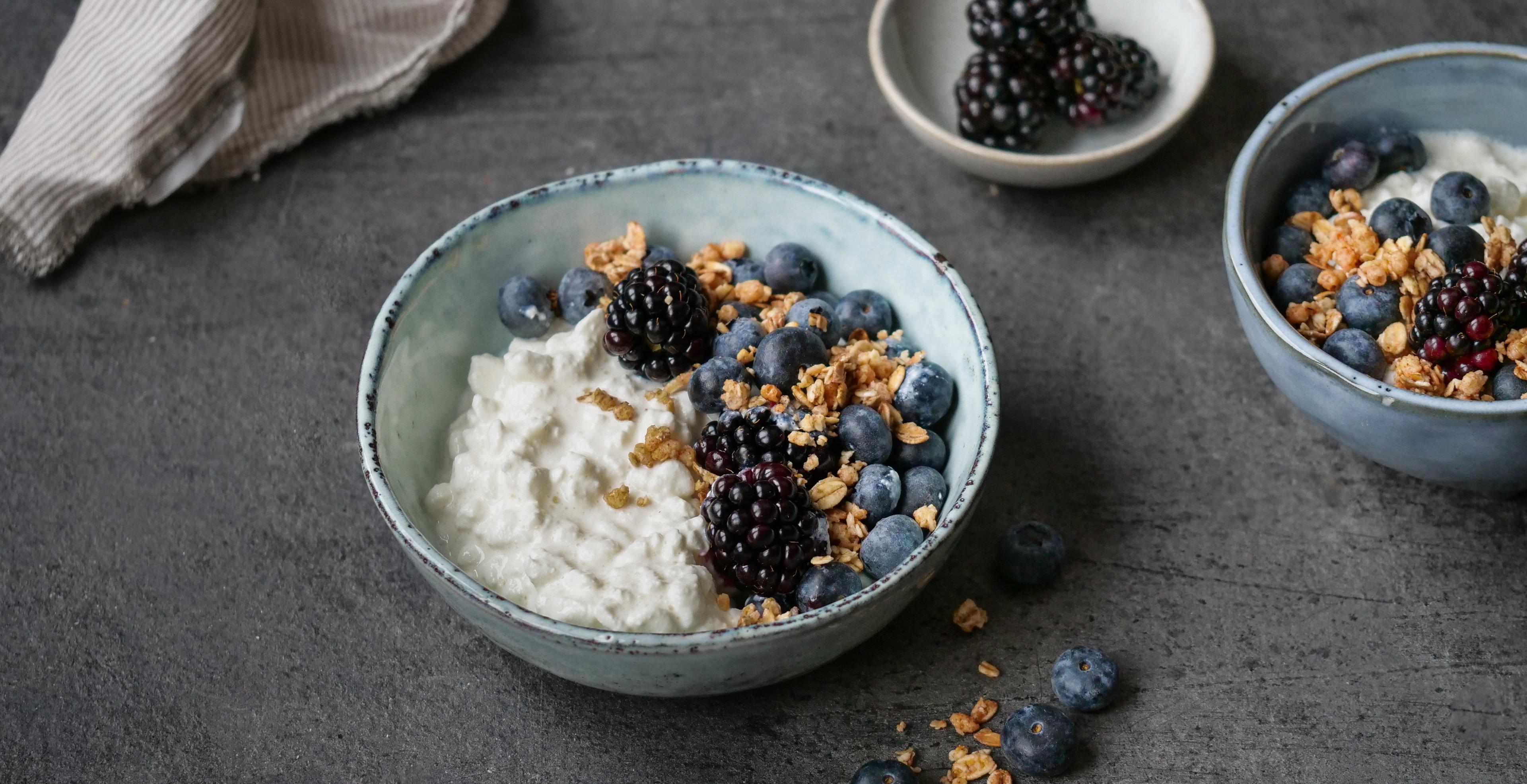 a bowl of yogurt with blueberries , blackberries and granola on a table .