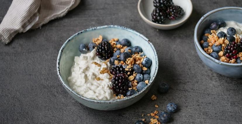 a bowl of yogurt with blueberries , blackberries and granola on a table .