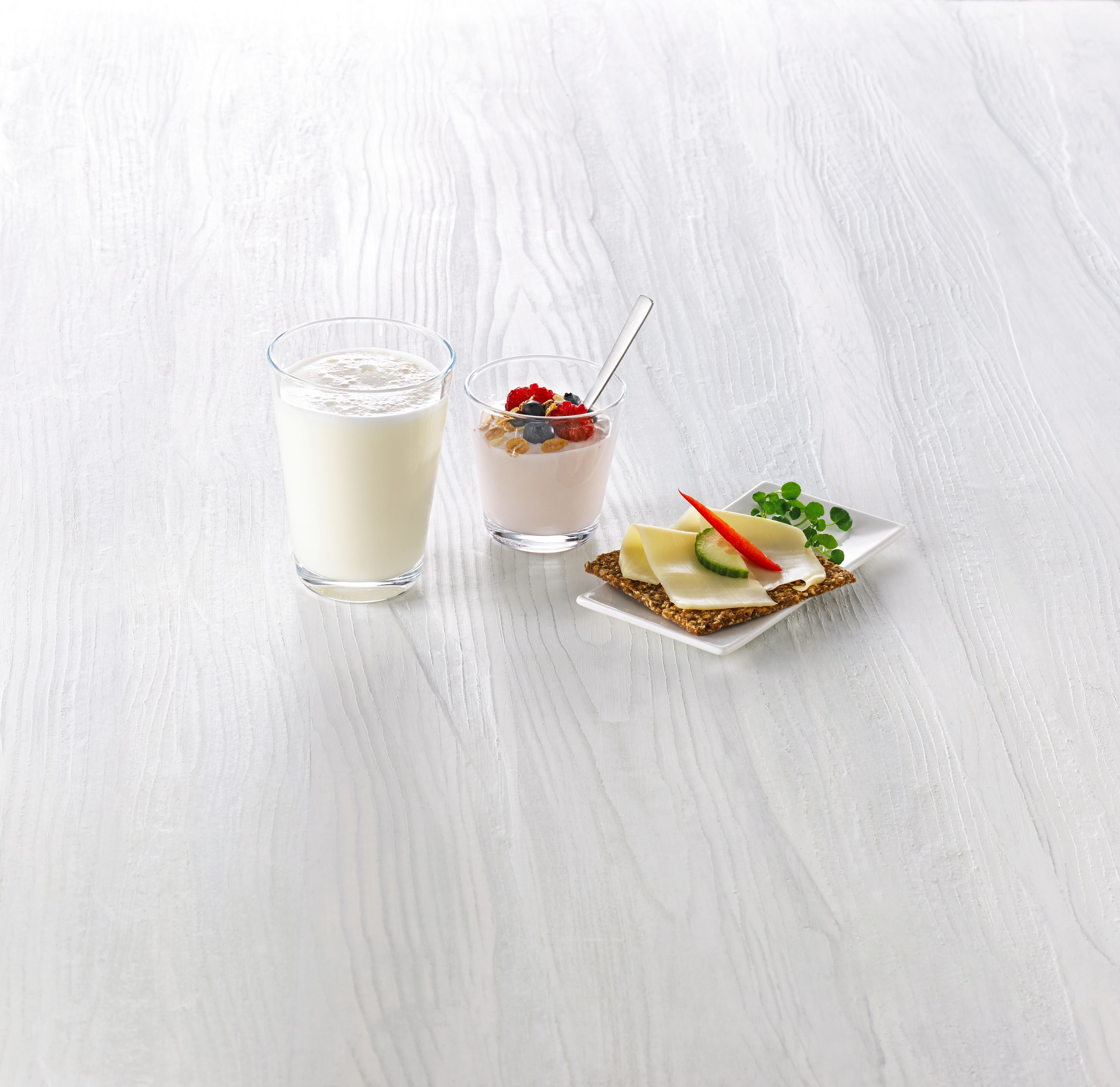 Ett glass melk, et beger yoghurt med litt müsli og friske bær, og ett knekkebrød med gulost, agurk og paprika.
