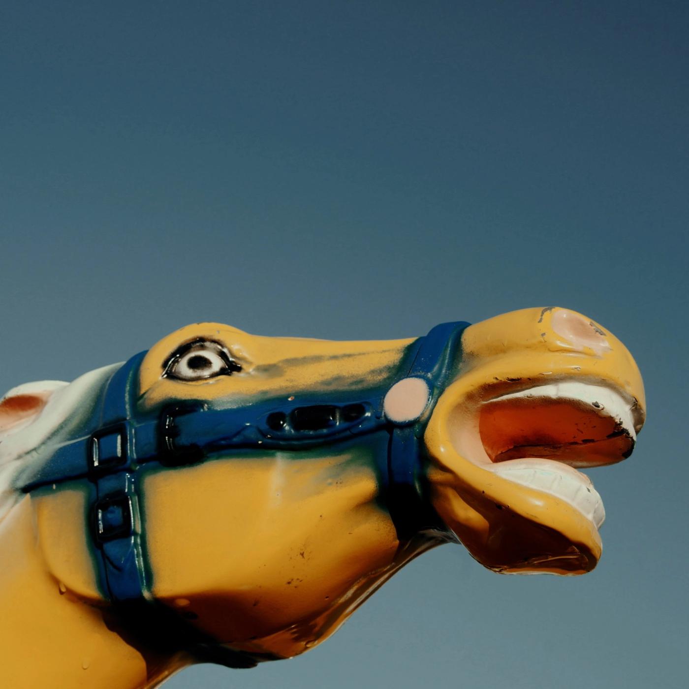 Y.O.T.H. single art: a yellow carousel horse head with a blue bridle and open mouth against a clear blue sky