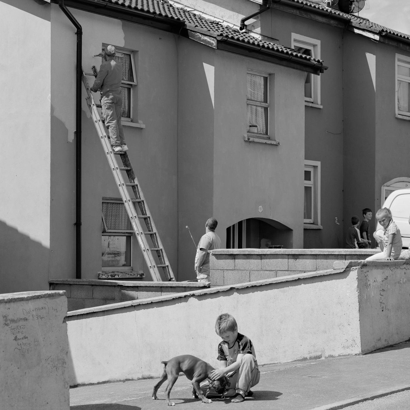 Single artwork for Aaron Rowe's Painter (Double-Edged Sword), a black and white street scene with a man on a ladder painting a house