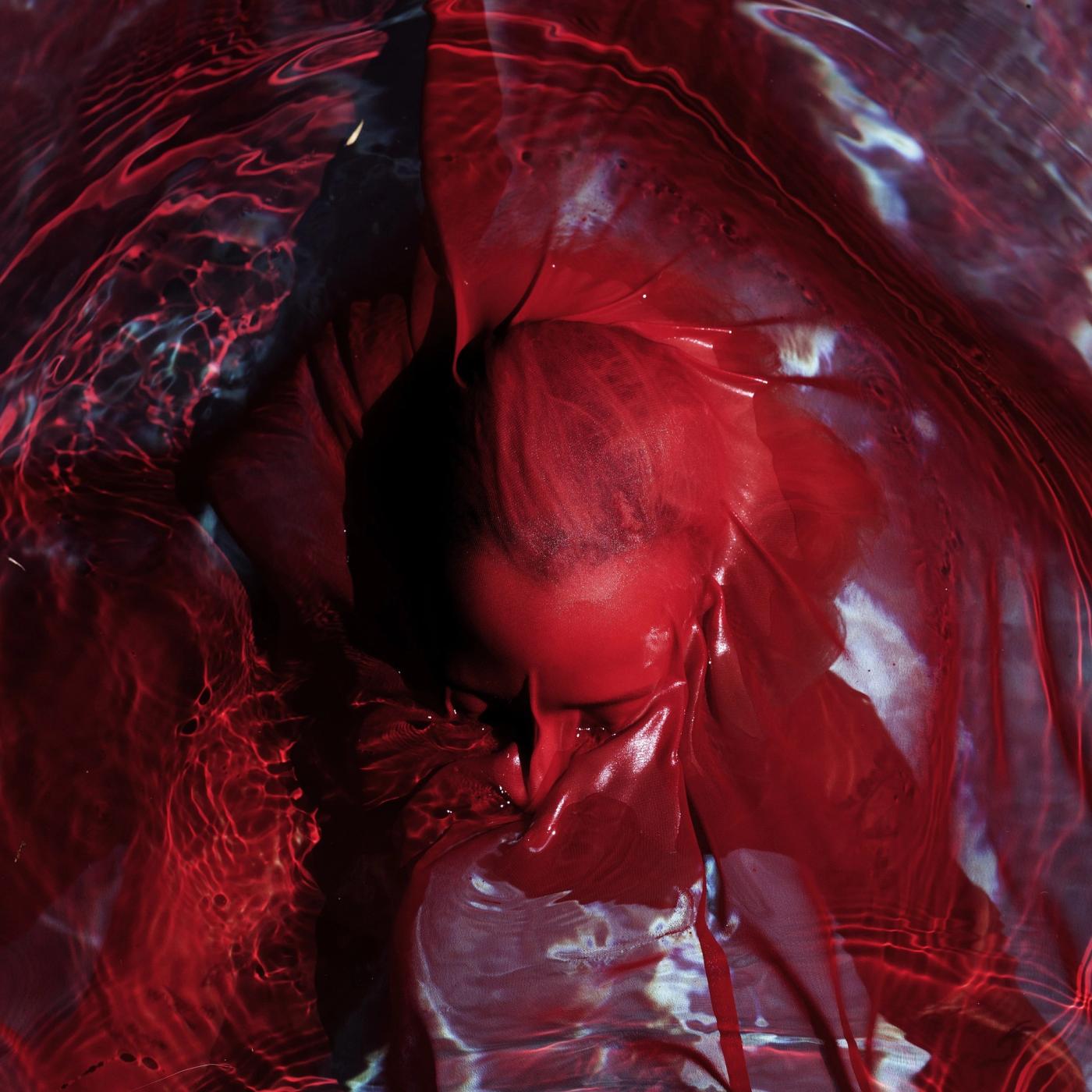 Not Here Not Gone album art: a figure seen through rippling red water, head bowed, face partly hidden by folds of red fabric