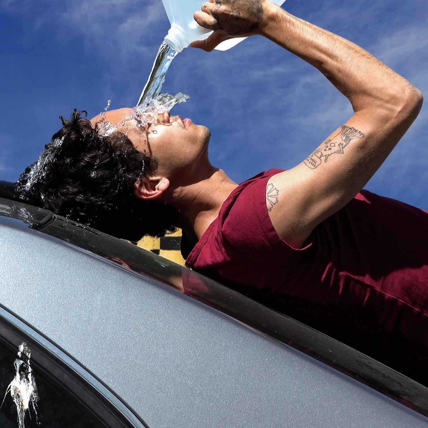 HOW TO QUIT SMOKING album cover: a man in a red T-shirt leans back against a silver car under a blue sky and pours water from a jug over his face.