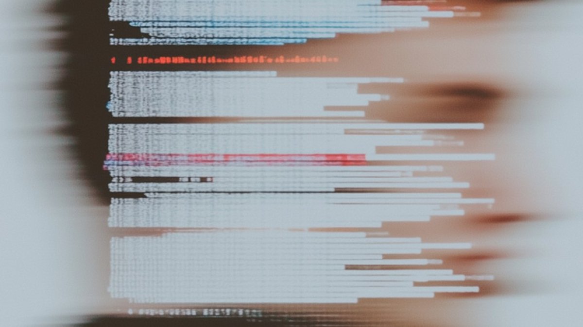 Abstract, blurred representation of computer source code with red and blue syntax highlighting, symbolizing the technical development of AI agents.