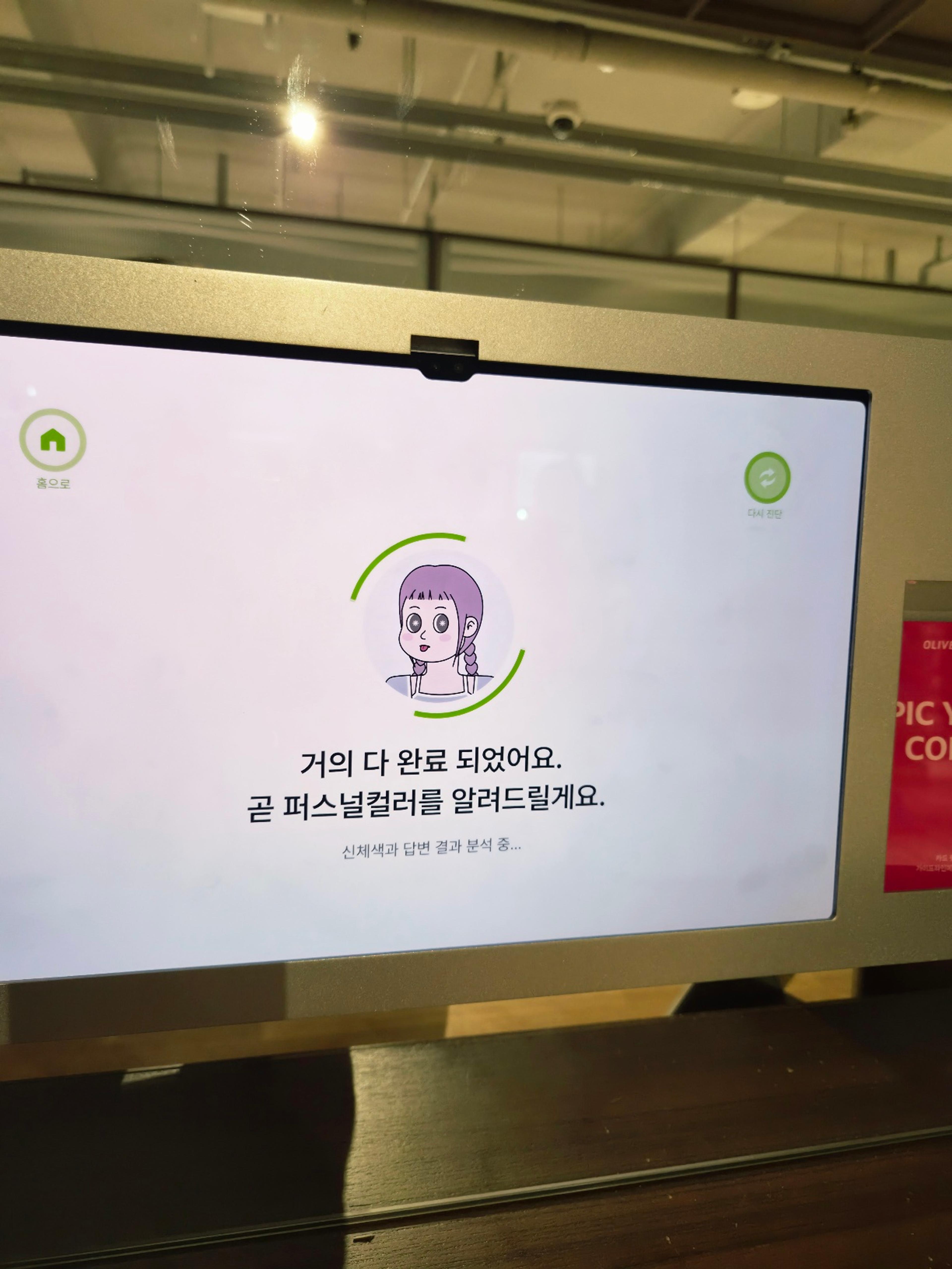 The kiosk screen showing a progress circle with a cute cartoon avatar and Korean text reading Almost Done.