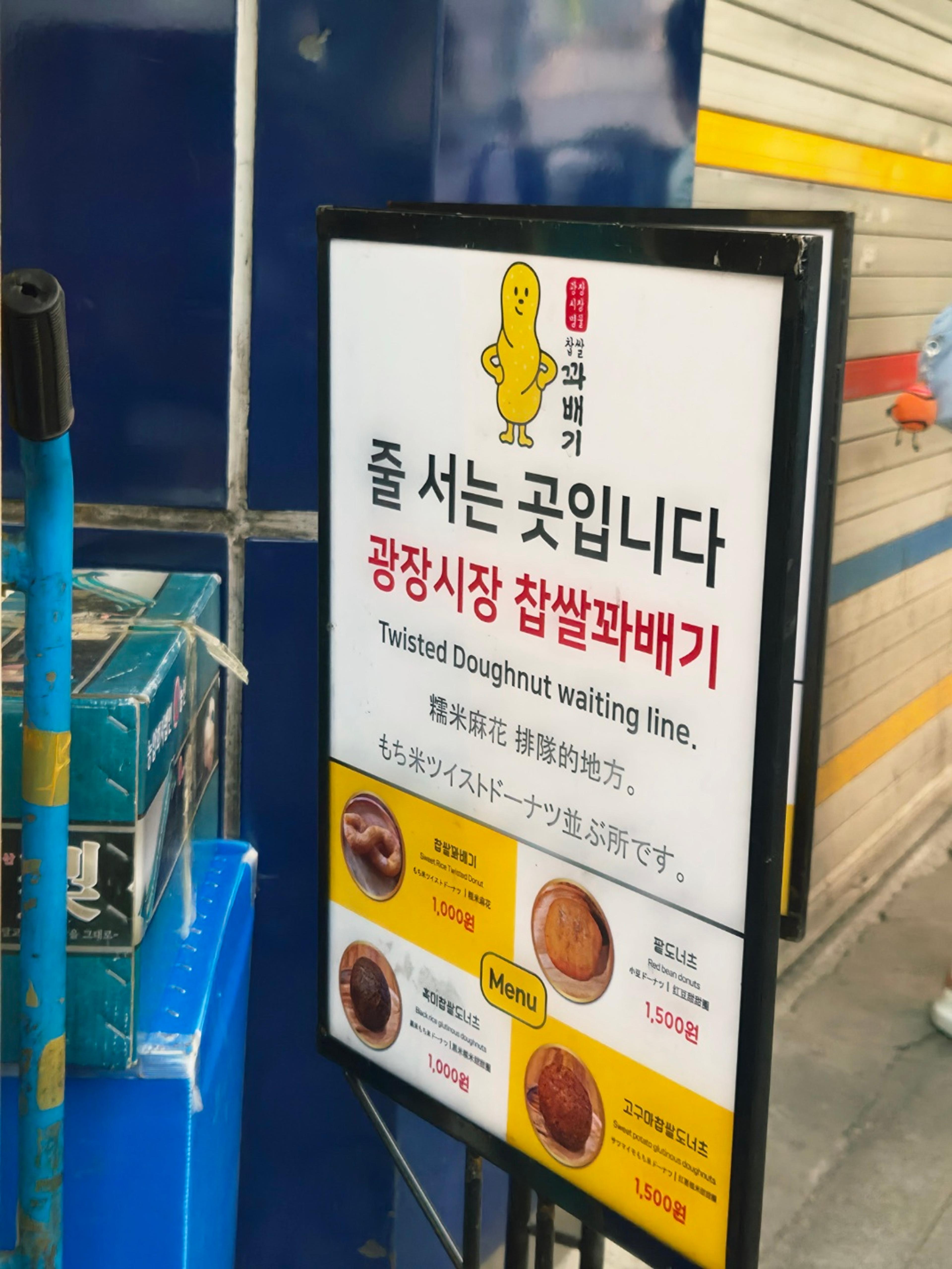 A white standing menu sign for the famous twisted doughnut shop with text reading Twisted Doughnut waiting line in English and Korean.