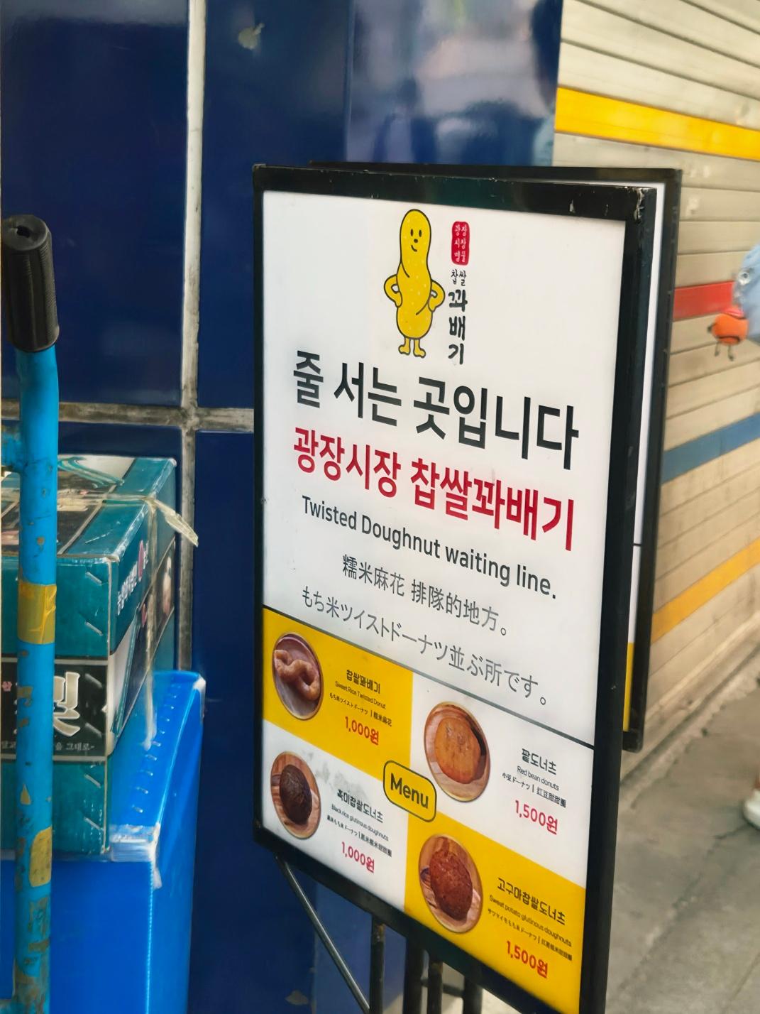 A white standing menu sign for the famous twisted doughnut shop with text reading Twisted Doughnut waiting line in English and Korean.
