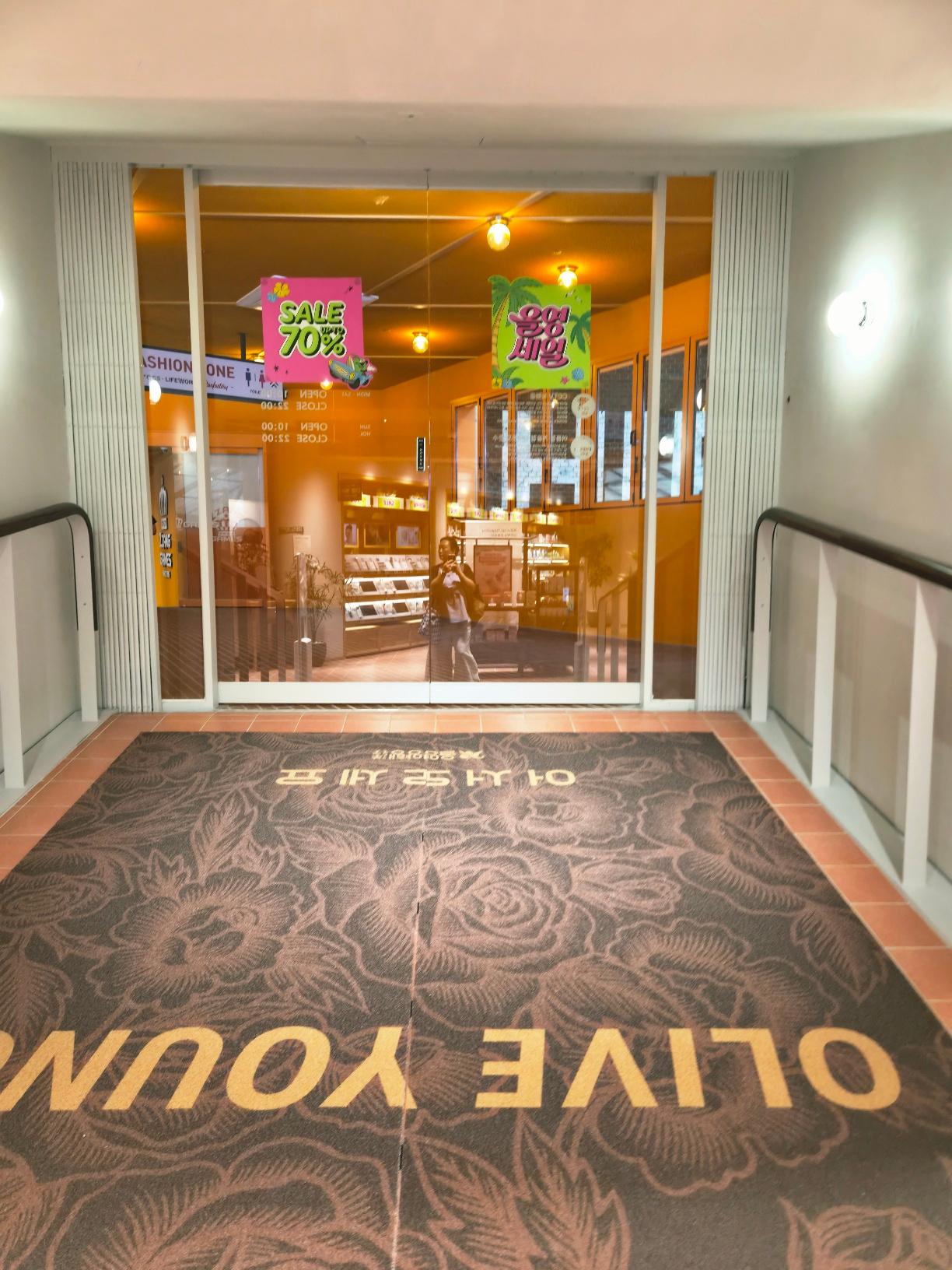 A premium brown floor mat with elegant rose patterns and gold Olive Young lettering at the store exit.