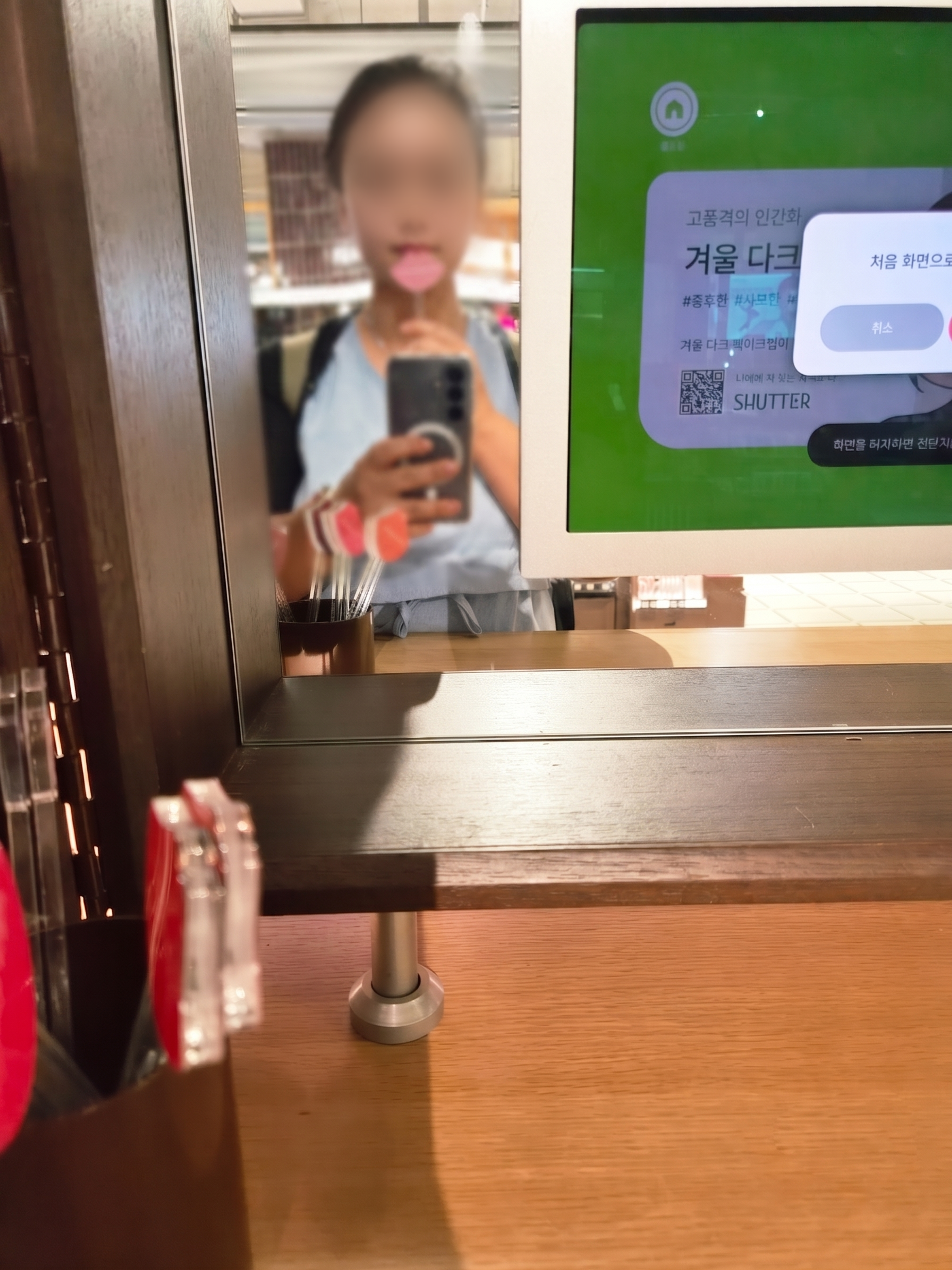 A close-up selfie in a vanity mirror showing a customer holding a clear pink lip-shaped color chip against their lips.