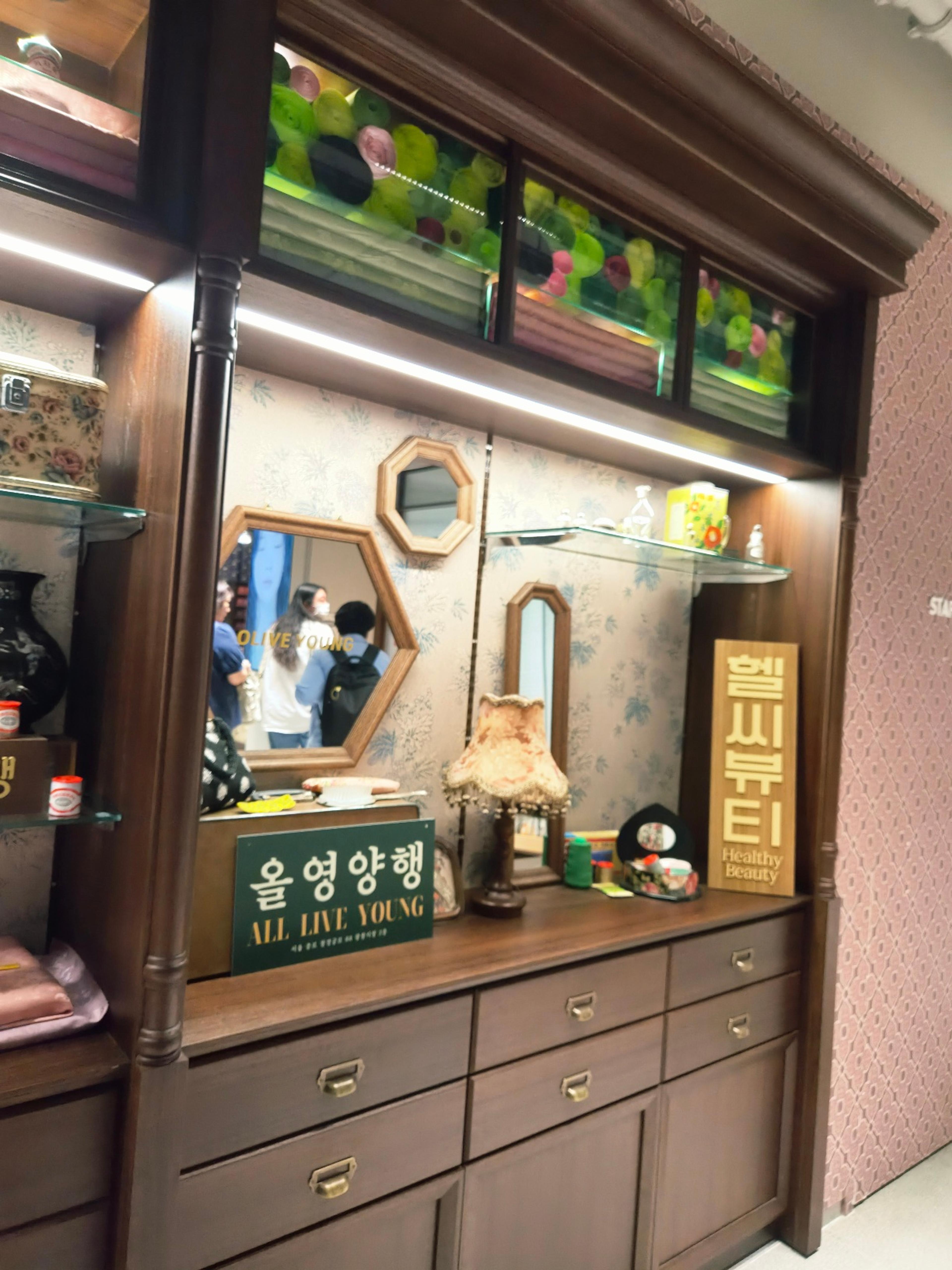 An elegant antique wooden vanity with geometric mirrors, a vintage fringed lamp, and retro product displays.