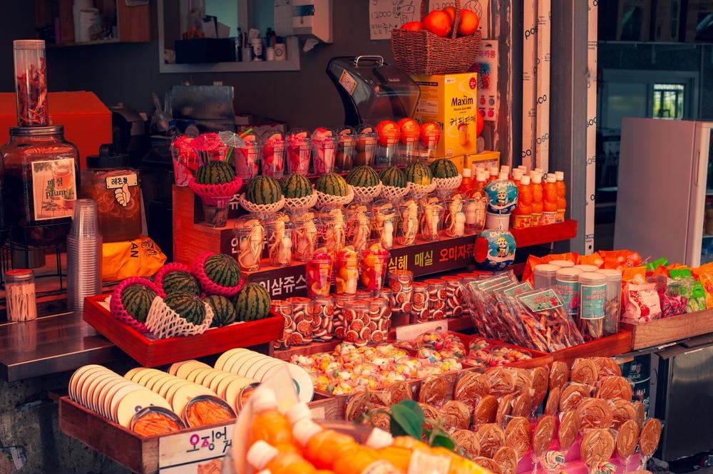 A vibrant street market stall filled with colorful snacks and fruit juices on a summer day