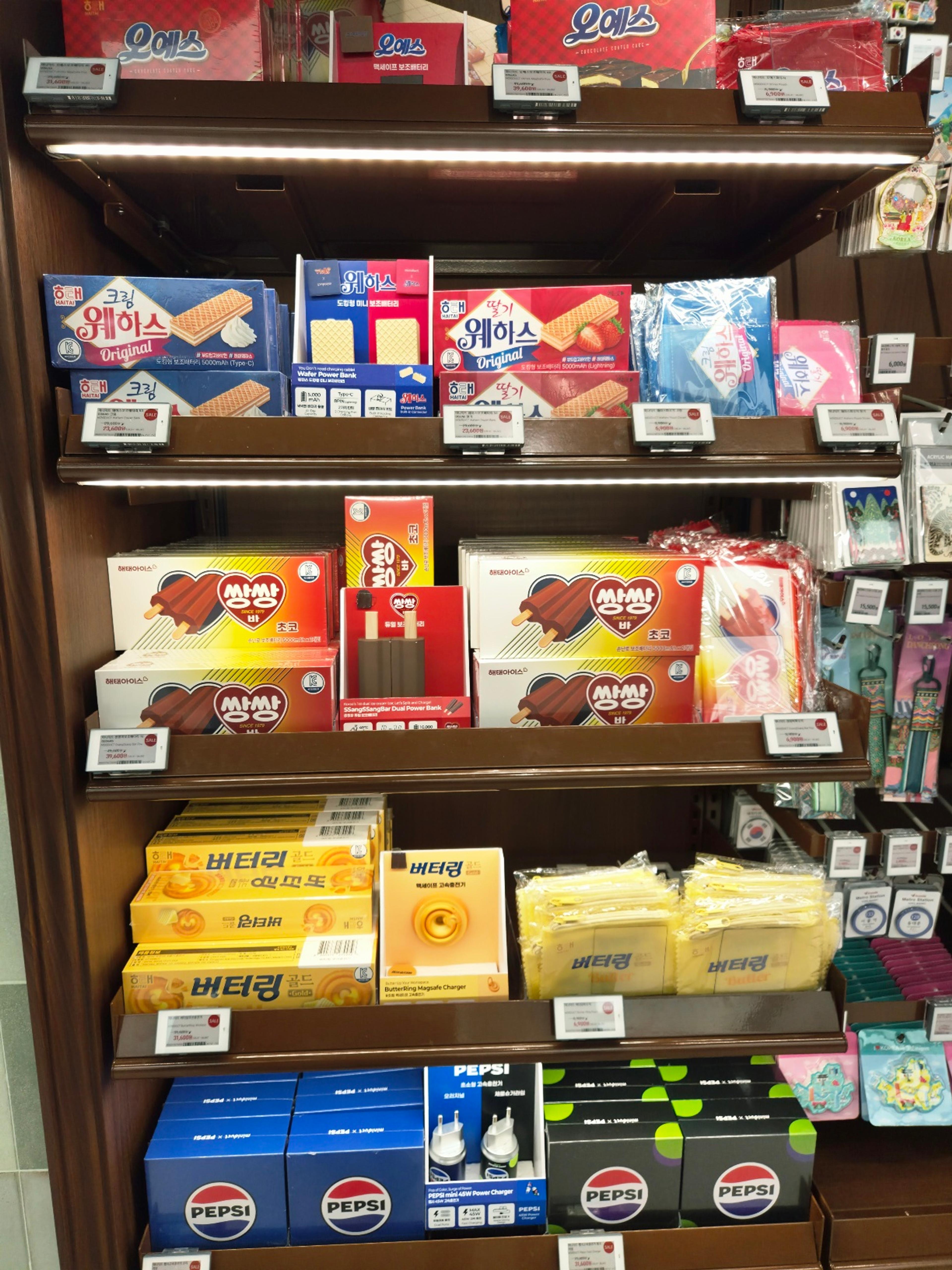 Store shelves showing a creative pairing of Korean snacks like wafers and Buttering cookies bundled with matching tech accessories like power banks and chargers.