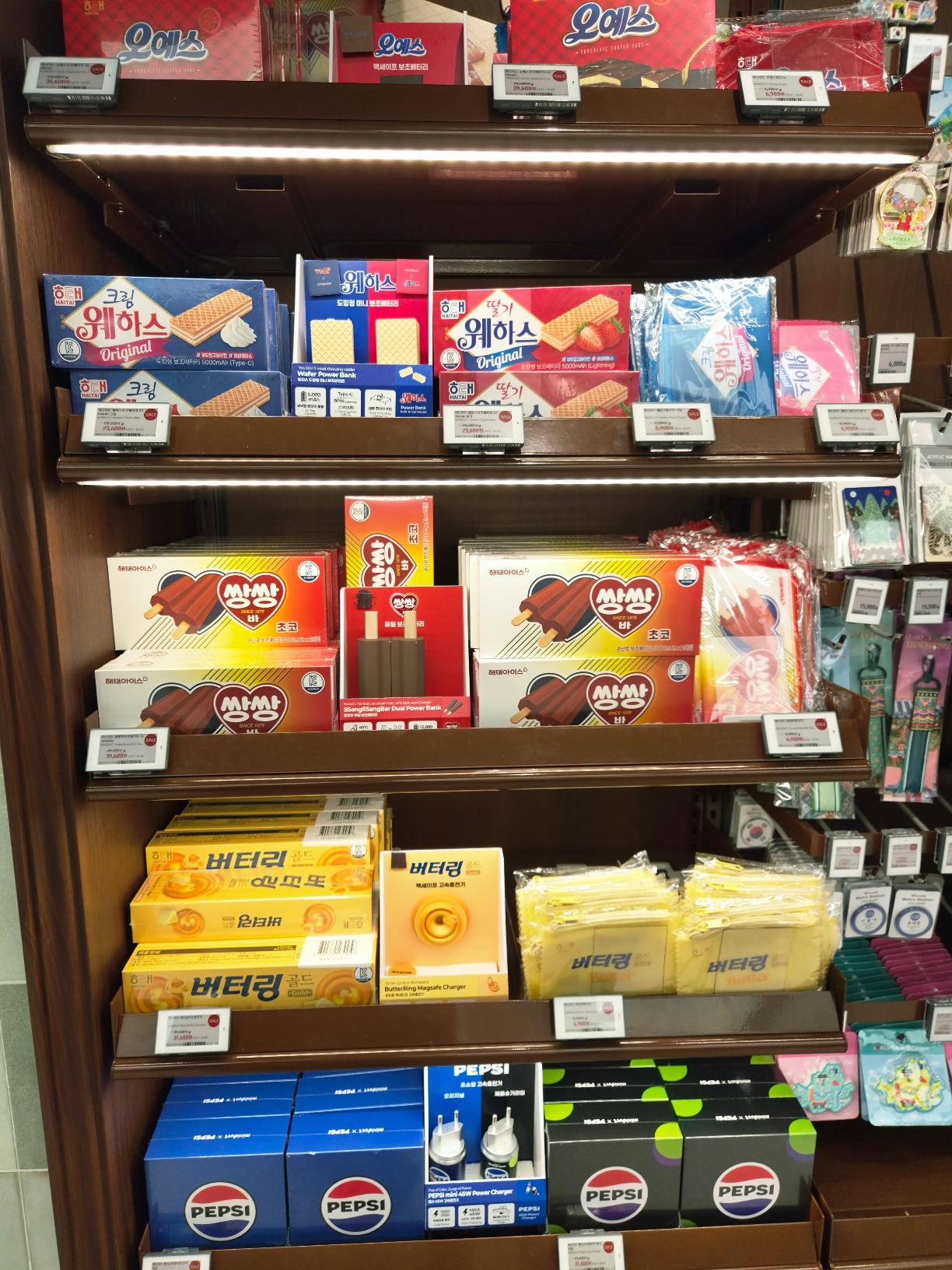 Store shelves showing a creative pairing of Korean snacks like wafers and Buttering cookies bundled with matching tech accessories like power banks and chargers.