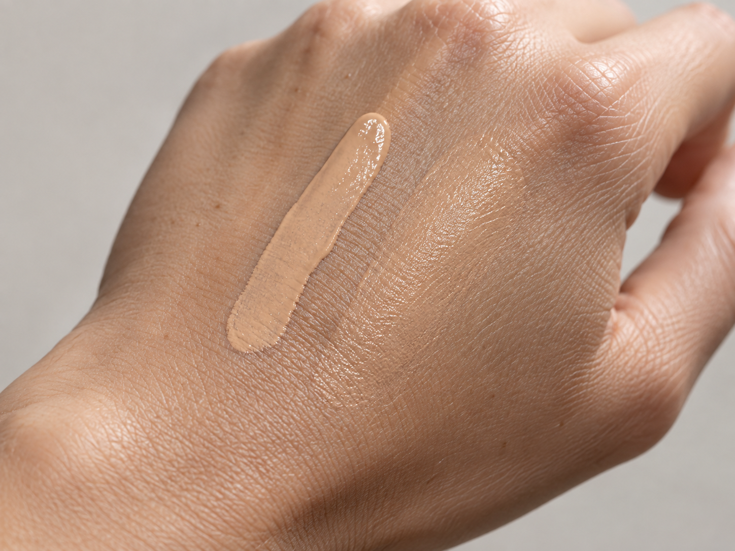 Two stripes of tinted base product blended on the back of a hand, one dewy and one blurred