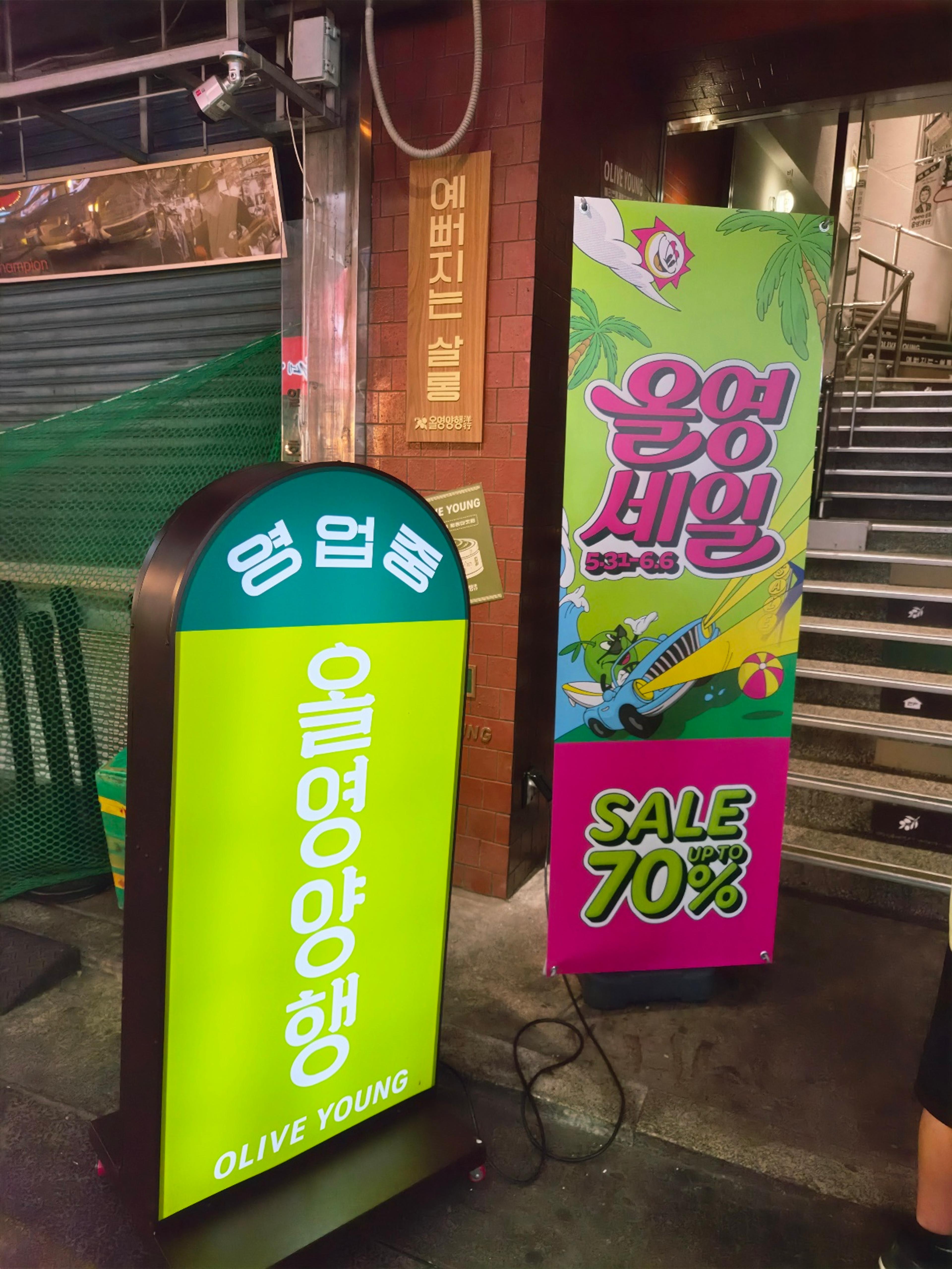 Olive Young Gwangjang Market branch entrance with a vibrant neon green and pink winter sale banner standing next to a retro light-up sign.