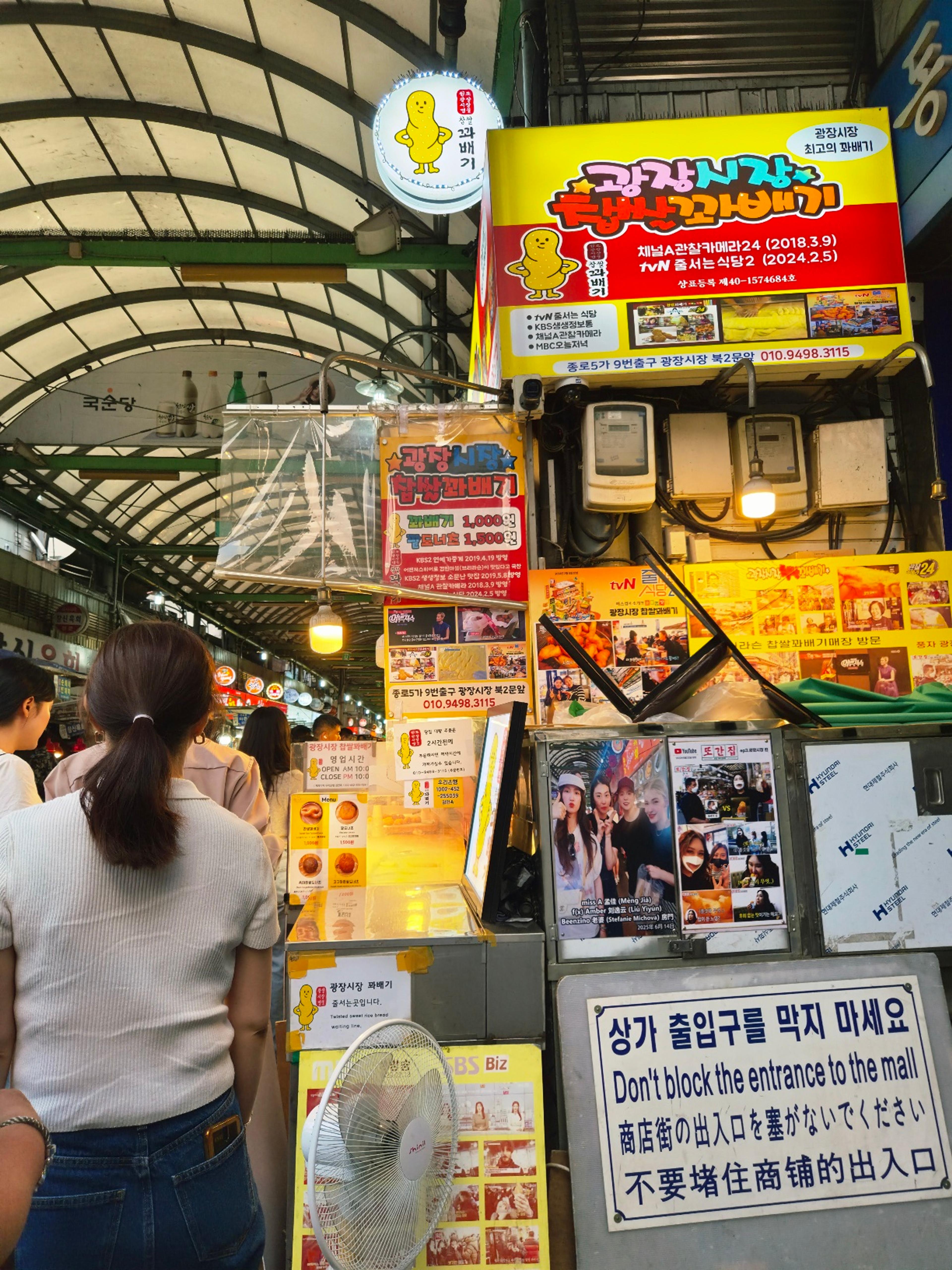 The famous yellow and red storefront of the Gwangjang Market twisted doughnut stall covered in TV broadcast clippings and celebrity photos.