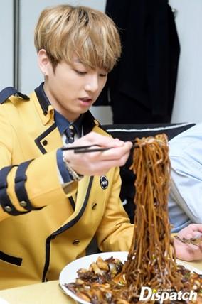 A student wearing a yellow school uniform lifts long strands of jajangmyeon with chopsticks