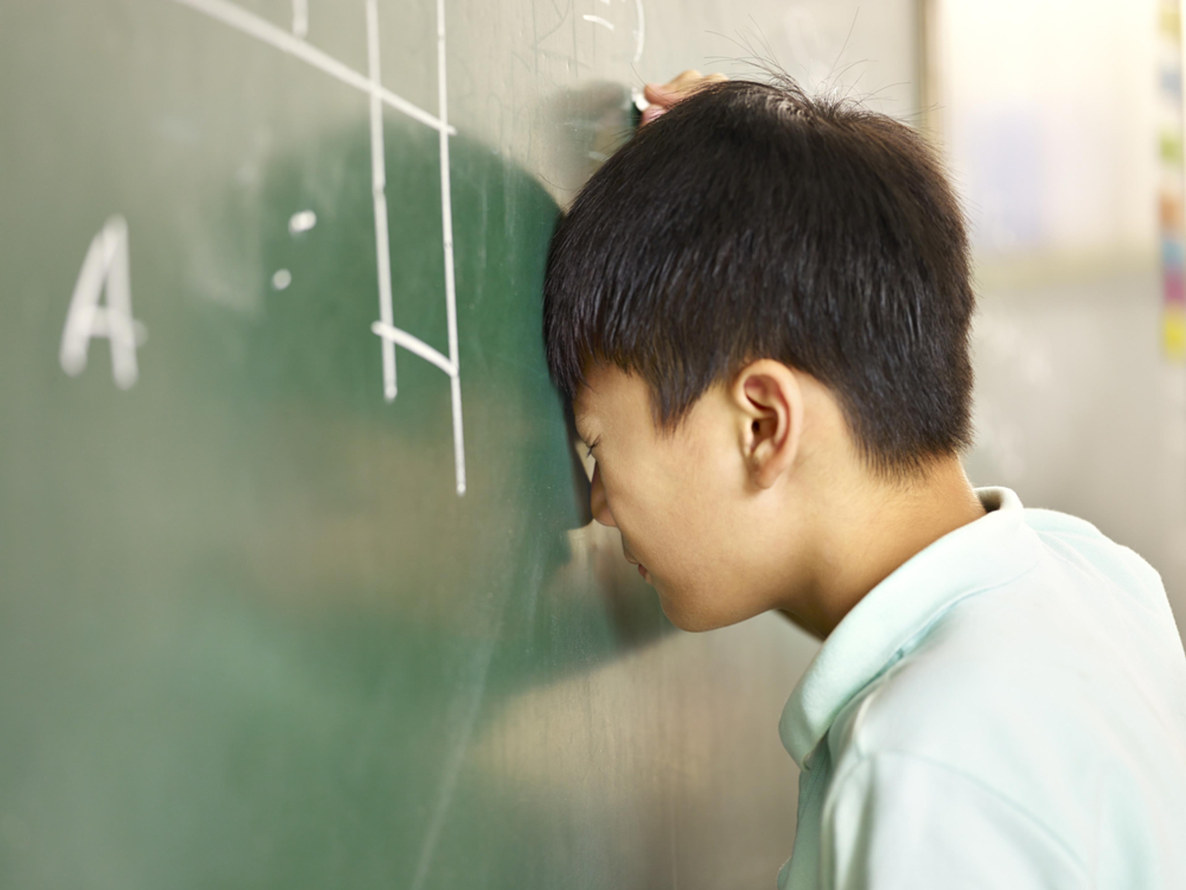 elementary schoolboy banging his head on blackboard