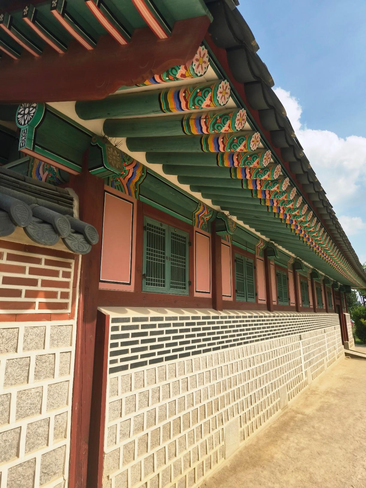 Close-up of Gyeongbokgung Palace roof corner with vibrantly painted dancheong wooden beams in green, orange, blue, and yellow against a cloudy sky