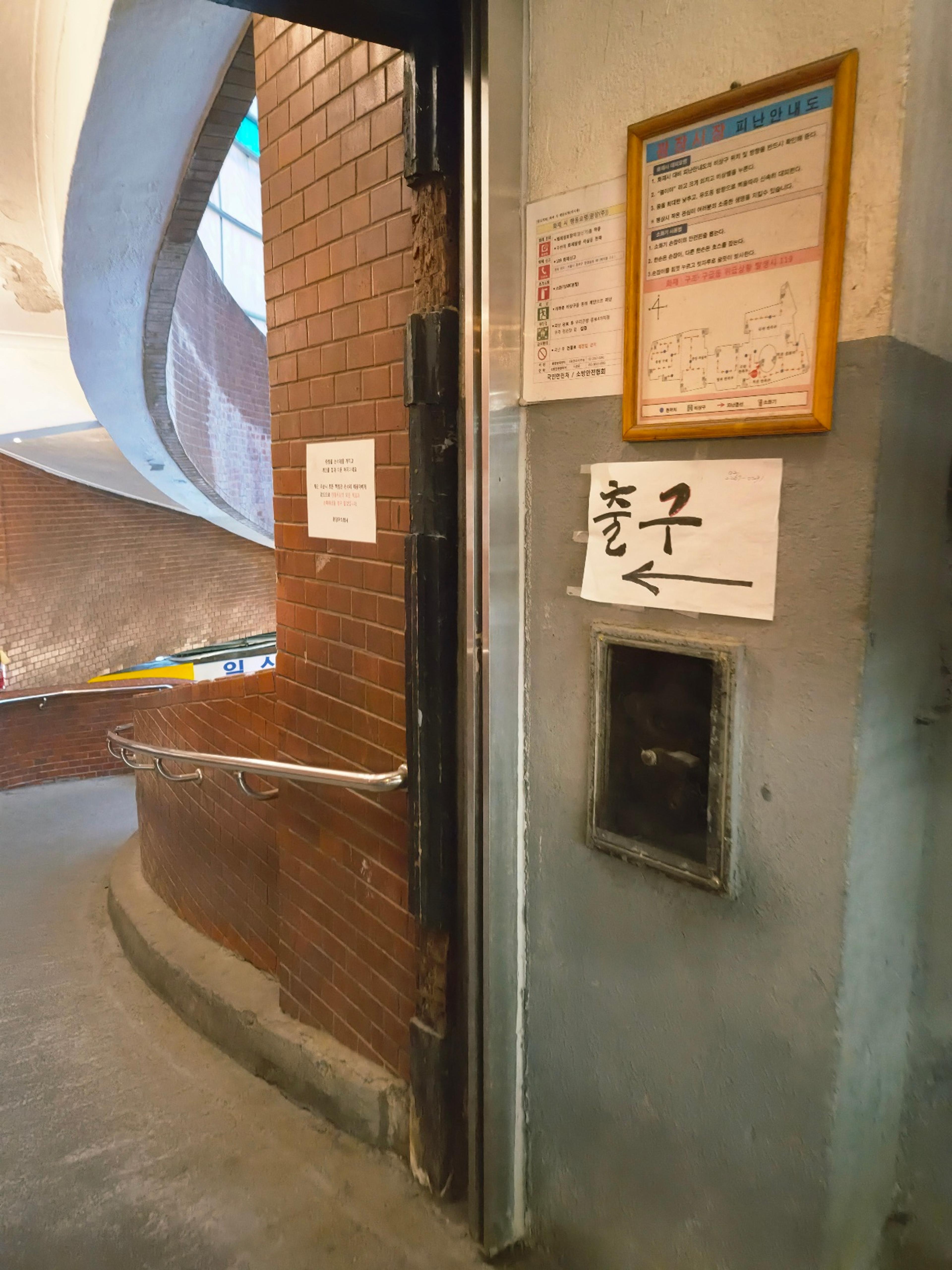 A close-up view of a grey concrete wall with an evacuation map and a white paper sign with an arrow pointing toward the Exit.