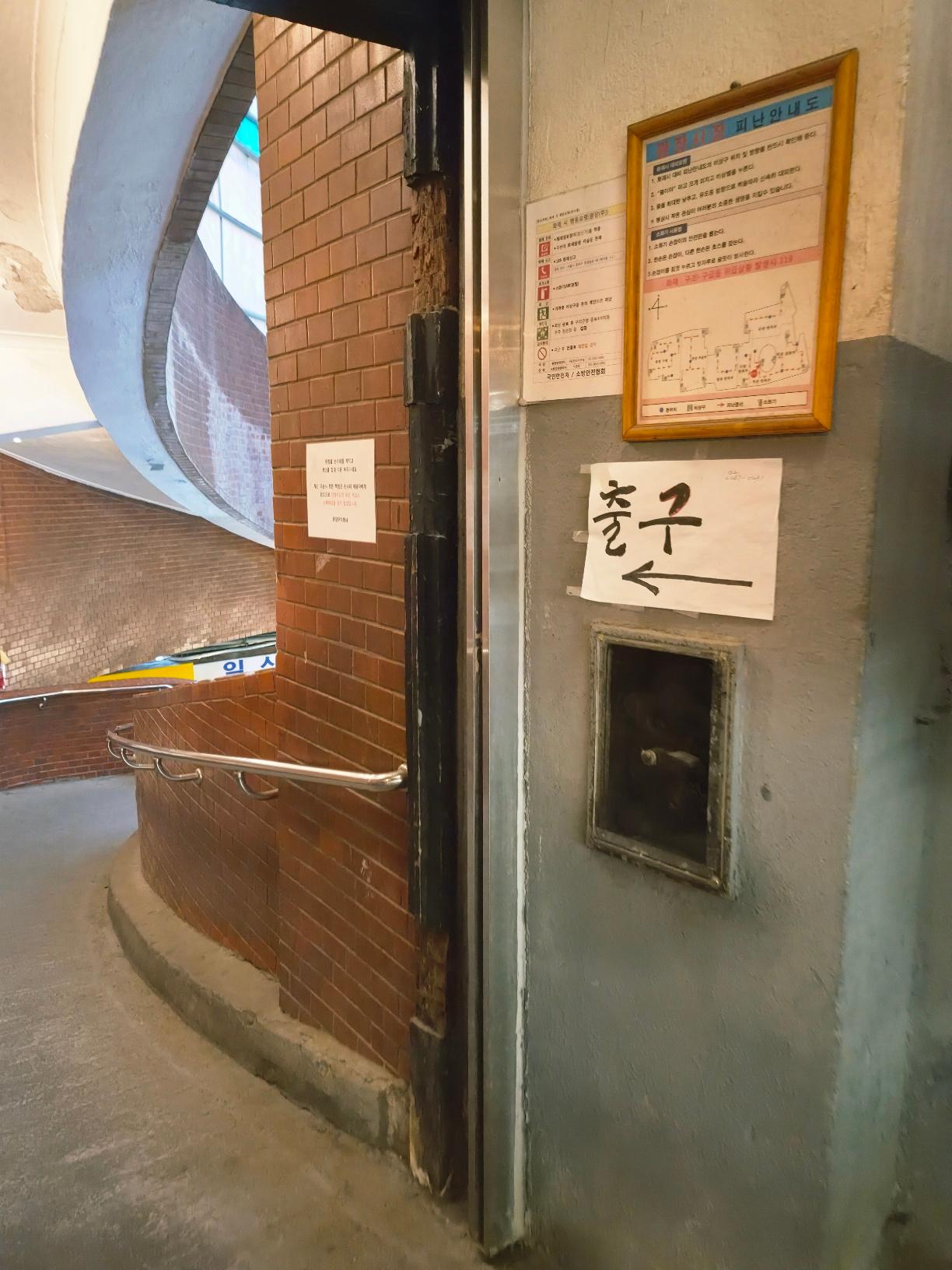 A close-up view of a grey concrete wall with an evacuation map and a white paper sign with an arrow pointing toward the Exit.