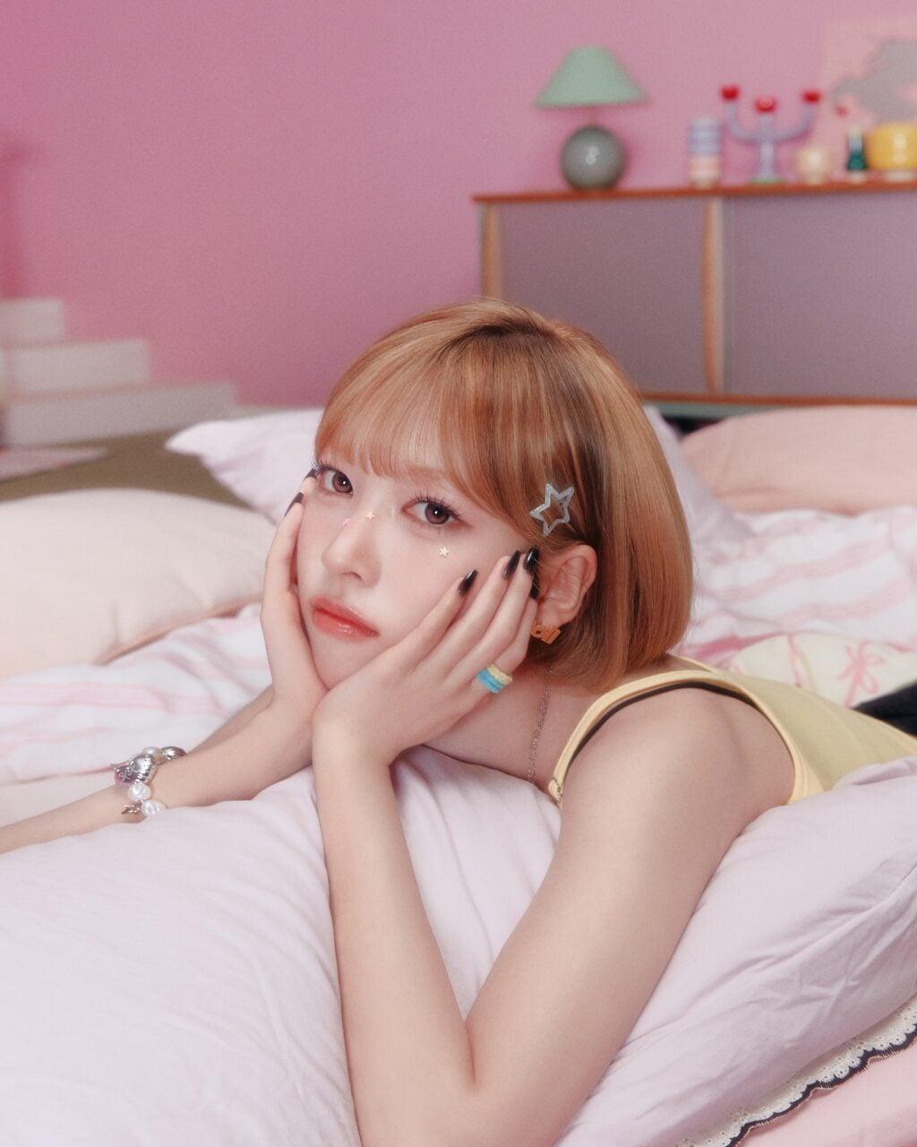 May of RESCENE resting her face in her hands on a pink bed in an official promotional portrait