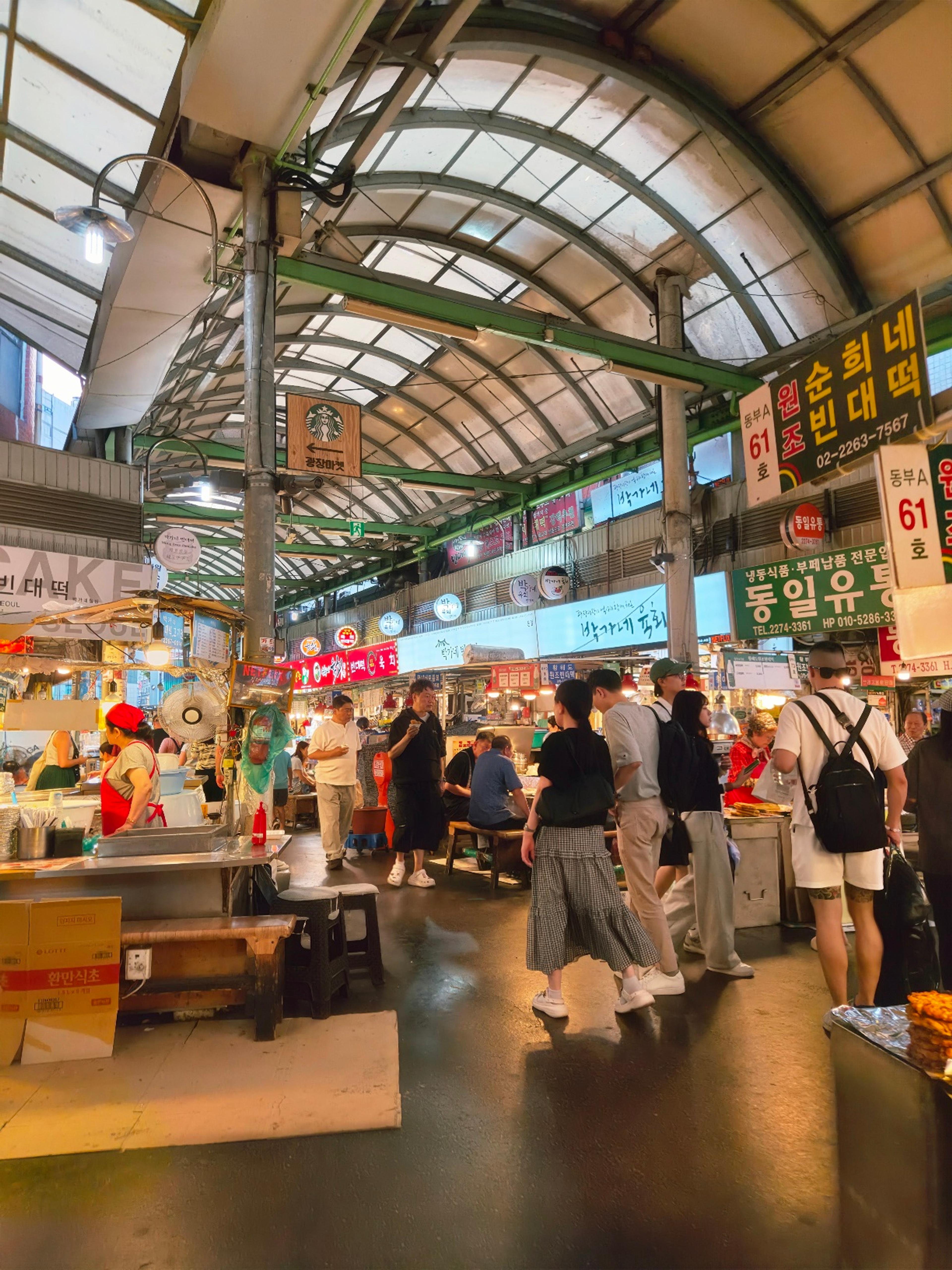 A bustling and lively traditional market food alley packed with vendors, overhead lights, and visitors walking through.