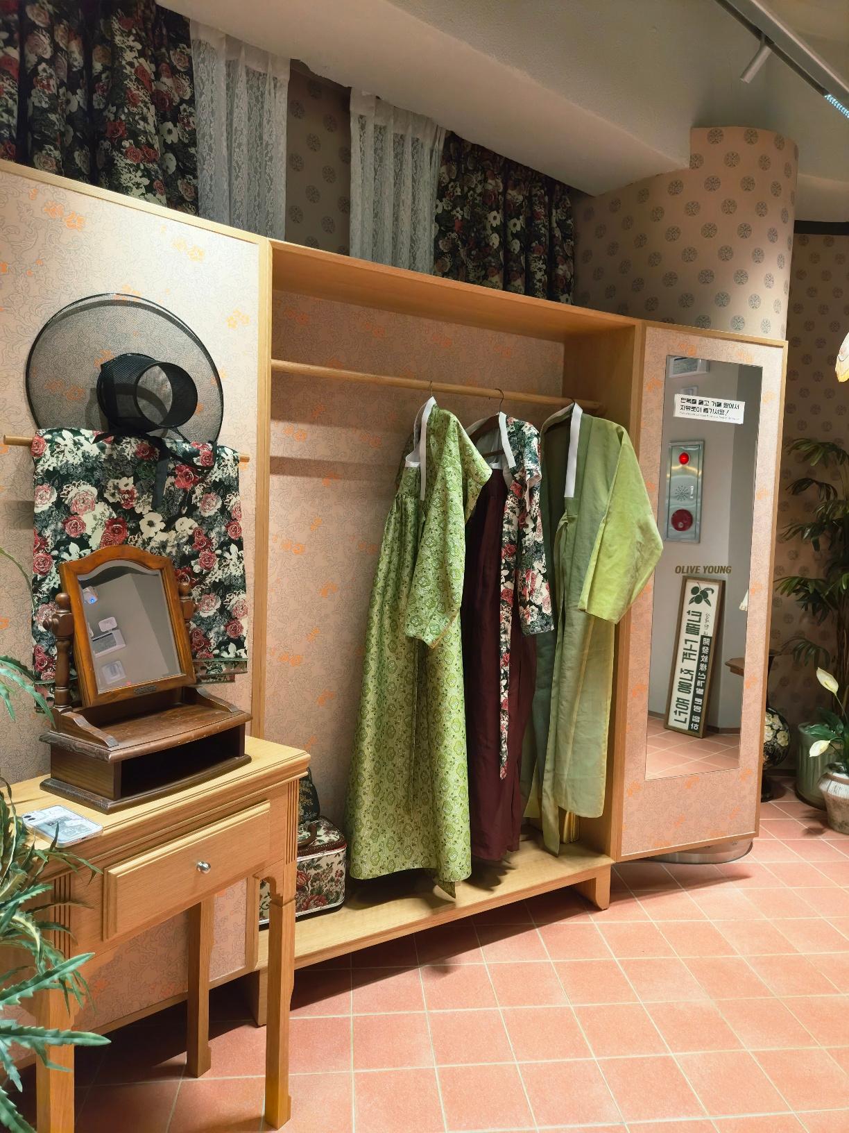 A traditional Hanbok dress-up booth inside Olive Young featuring green silk robes and a vintage wooden vanity mirror.